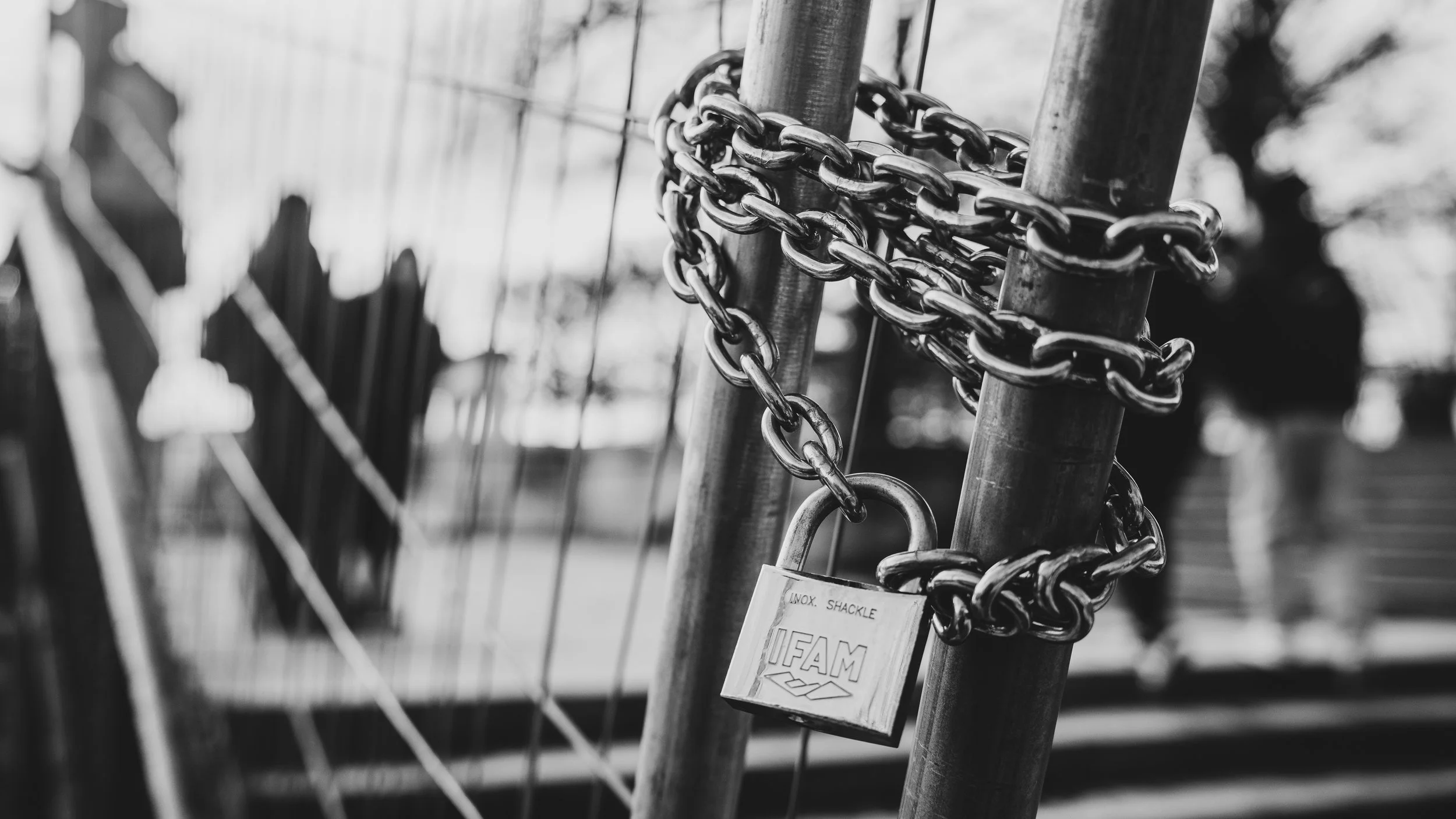 Black and white photo of a chain and padlock securing a metal gate or fence.