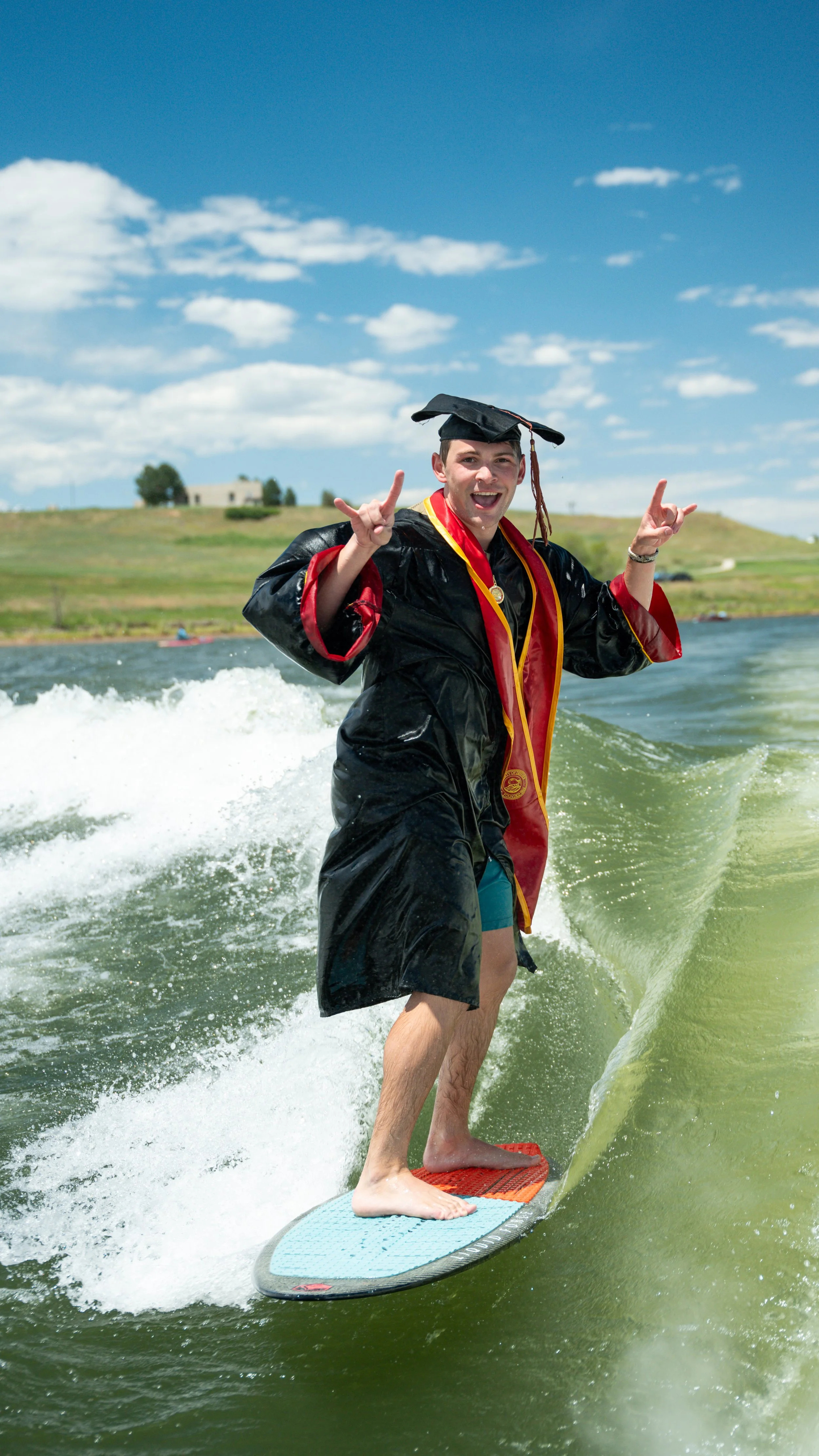 Happy graduate in cap and gown surfing on a wave on a sunny day