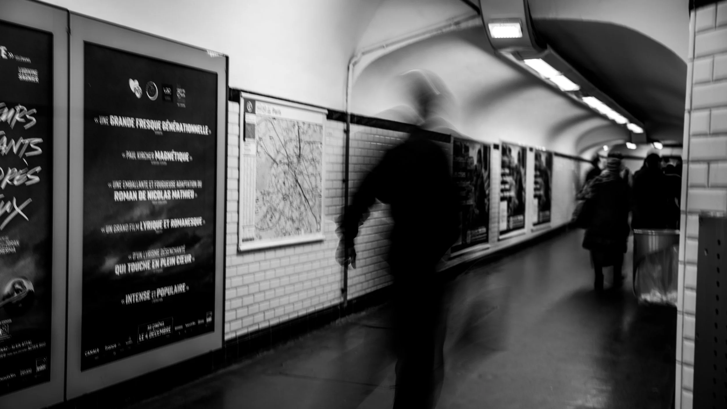 People walking through a subway station with posters on the walls and tiled columns.