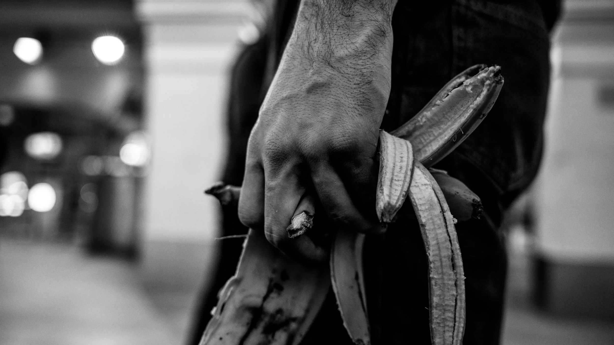 A person holding a banana peel and banana in their hand, with the background out of focus.