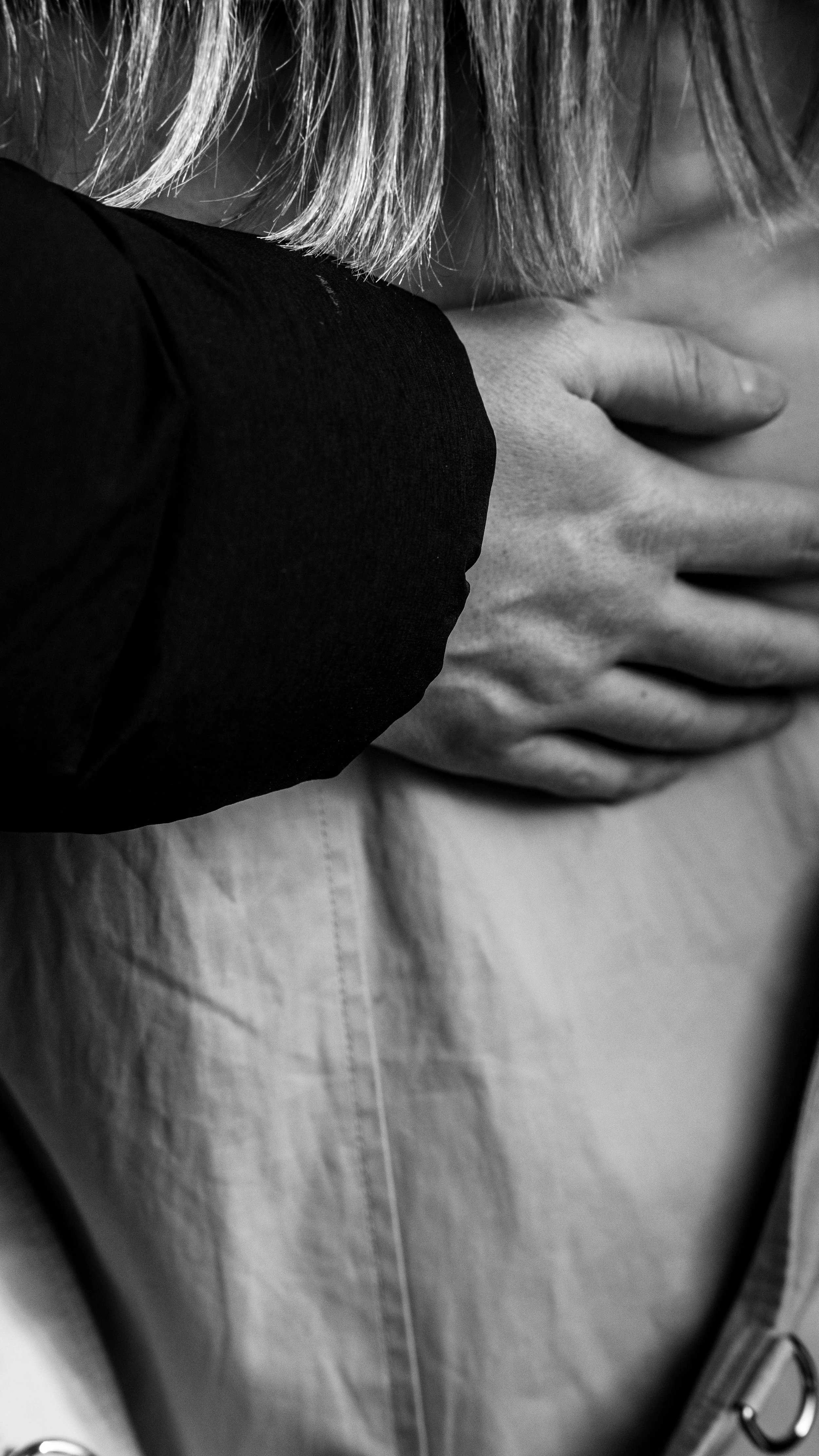 Close-up of a person's hand resting on their chest, with part of their face and hair visible, in black and white.