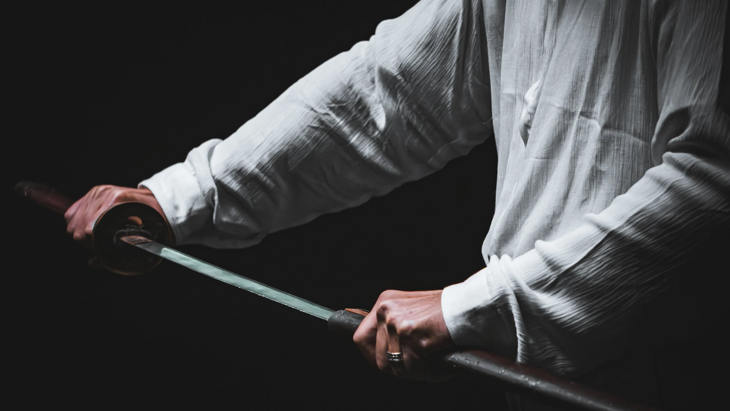 Person in a white shirt holding a sword or katana, with a dark background.