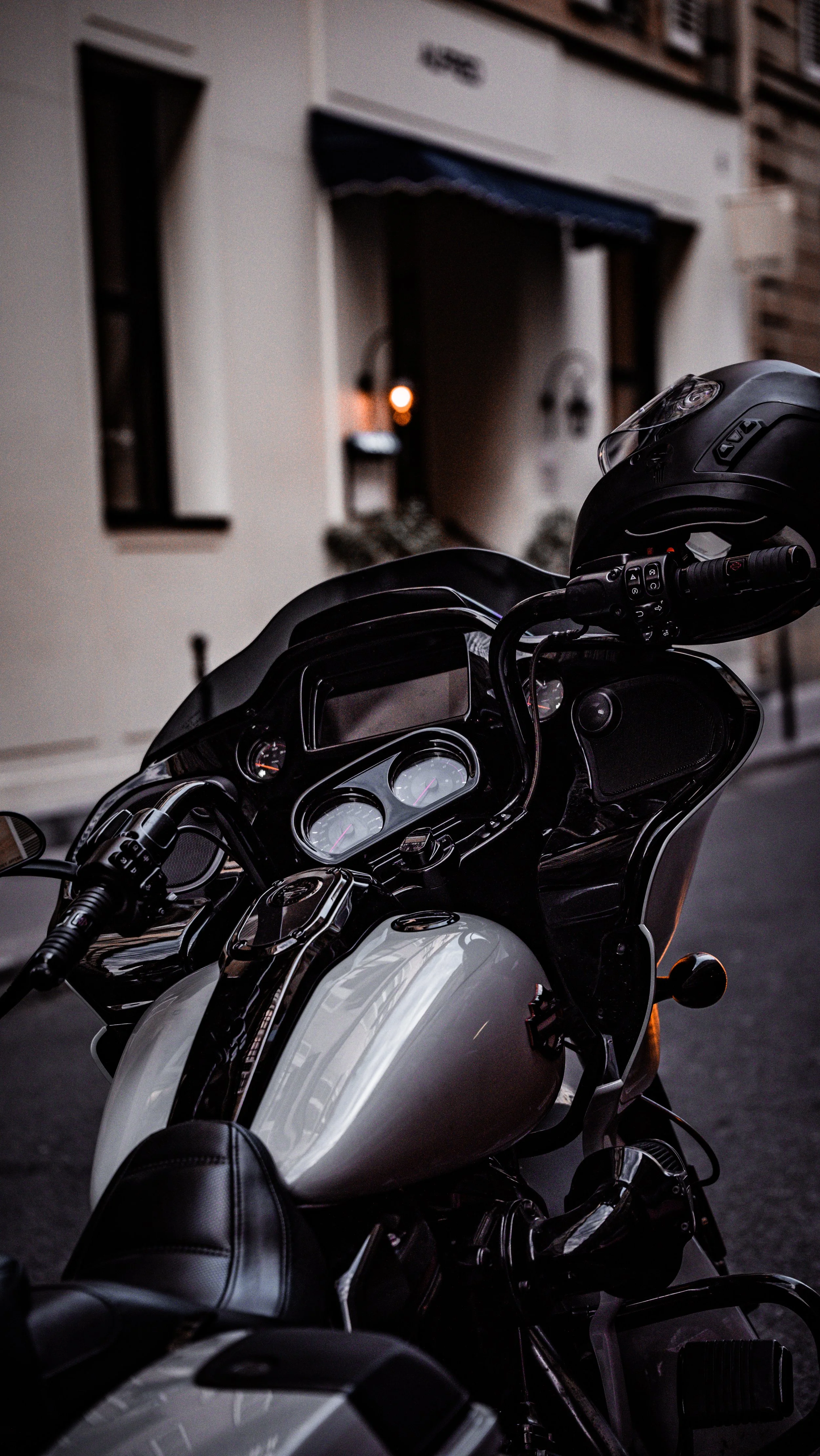 Close-up of a black and white motorcycle parked on a city street at dusk with a building in the background.