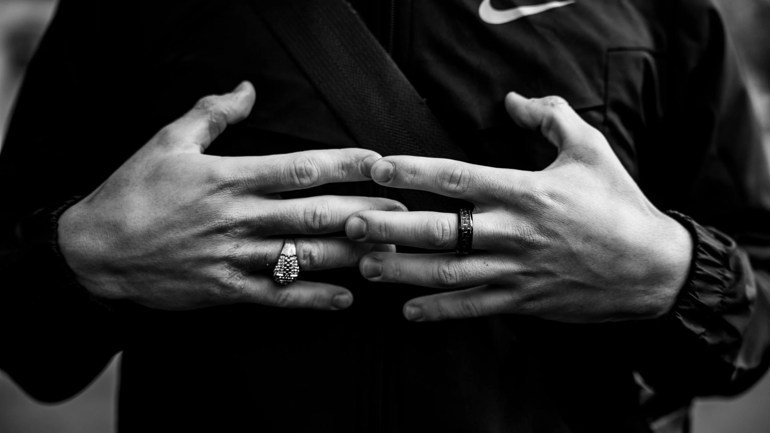 Close-up of a person's hands with rings, crossed over their chest, in black and white.