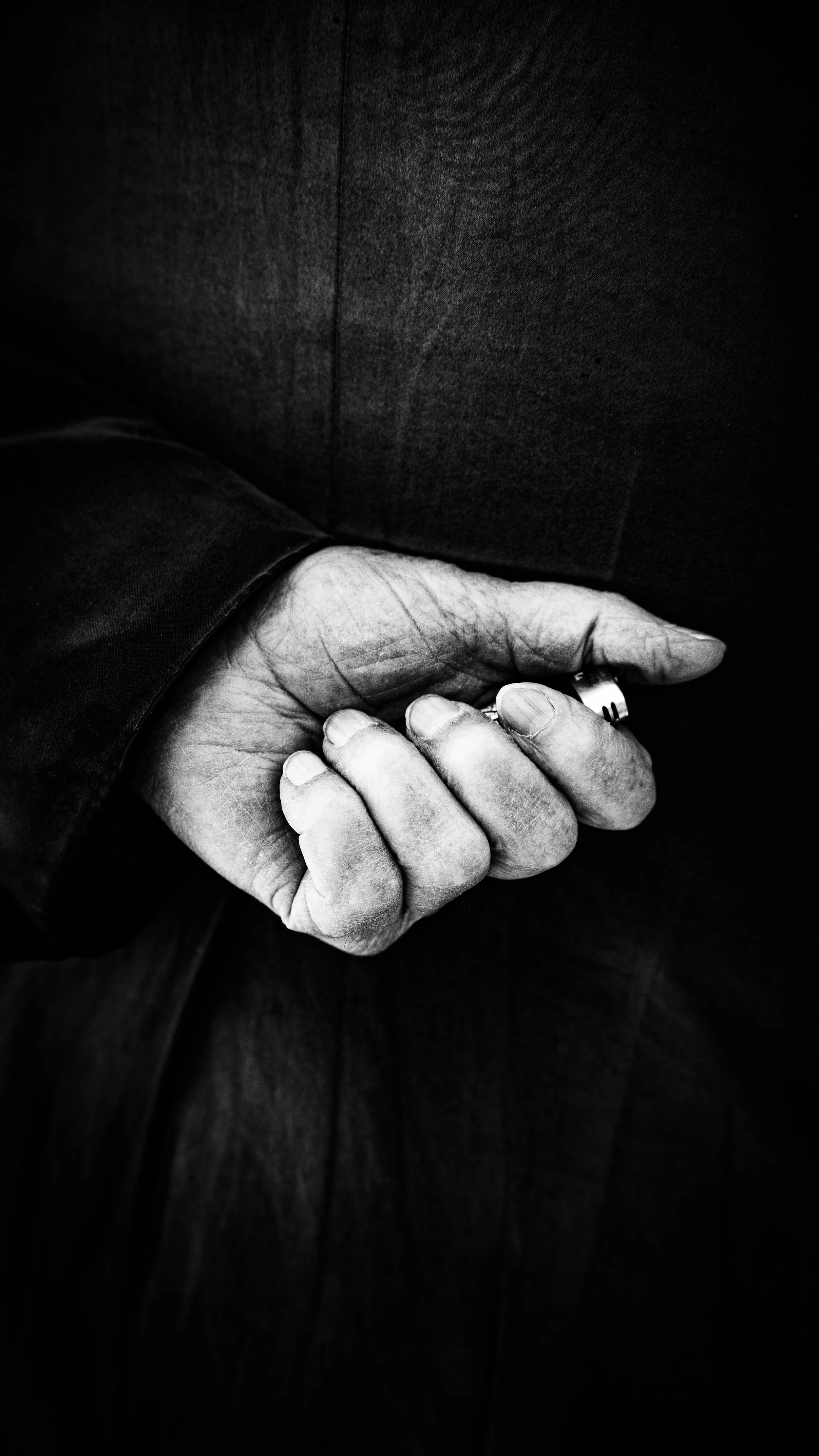 Close-up of a person's hand clenched into a fist, wearing a ring, with a dark suit jacket visible.