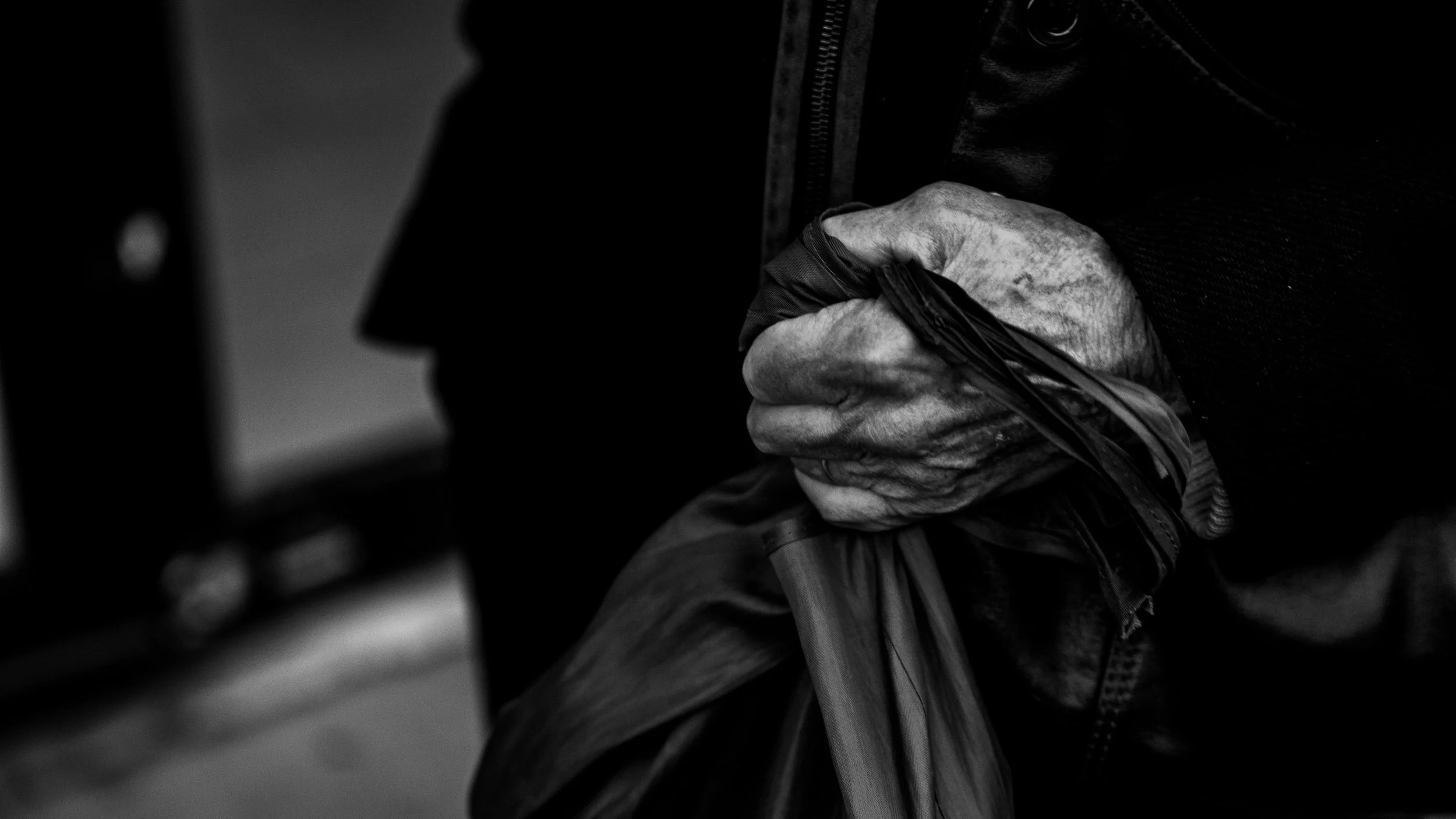 Close-up of elderly person's worn hand gripping a plastic bag, black and white