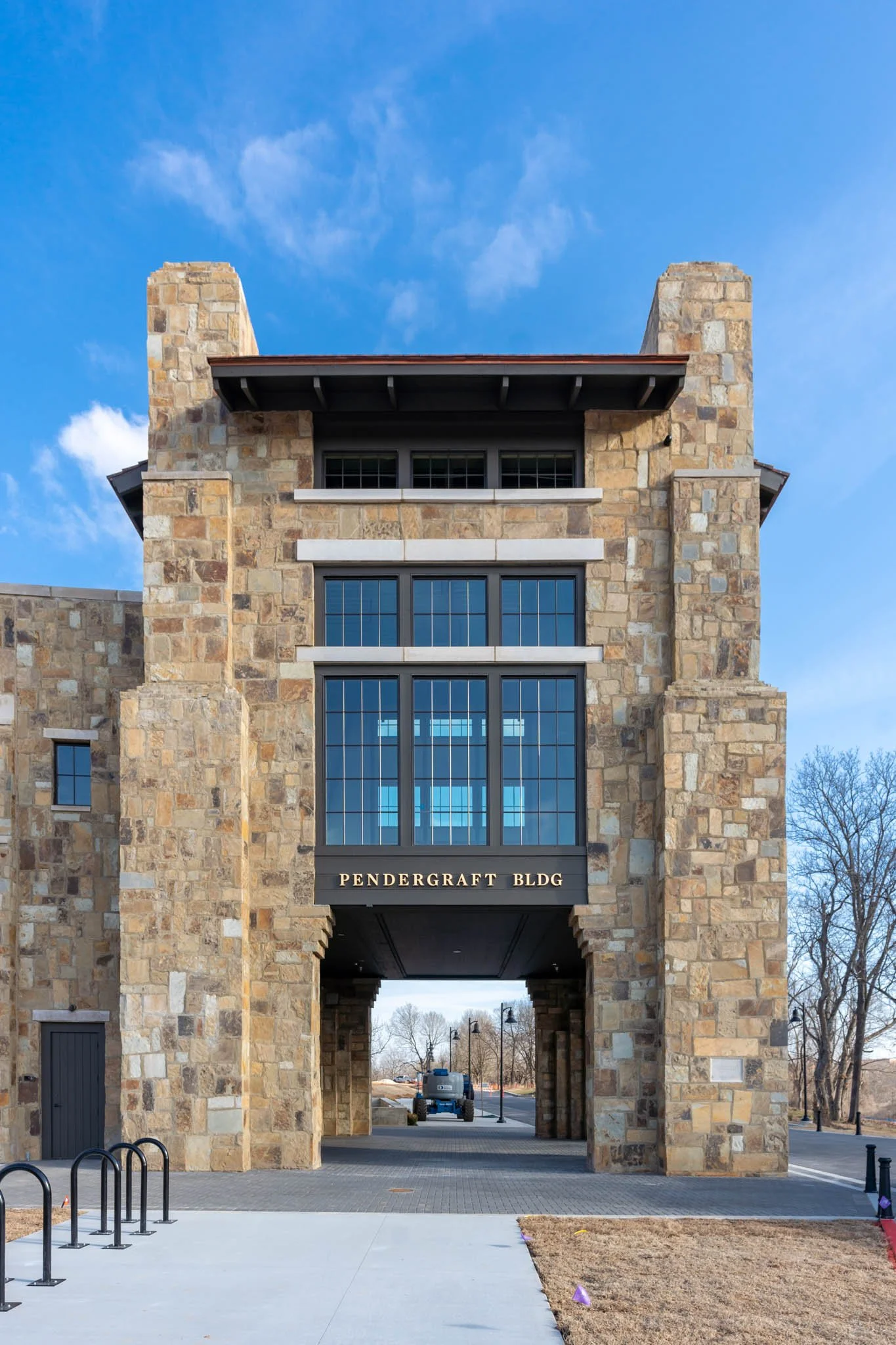 Stone building with an archway entrance, labeled "Pendergraft BLDG," featuring large windows and a blue sky in the background.