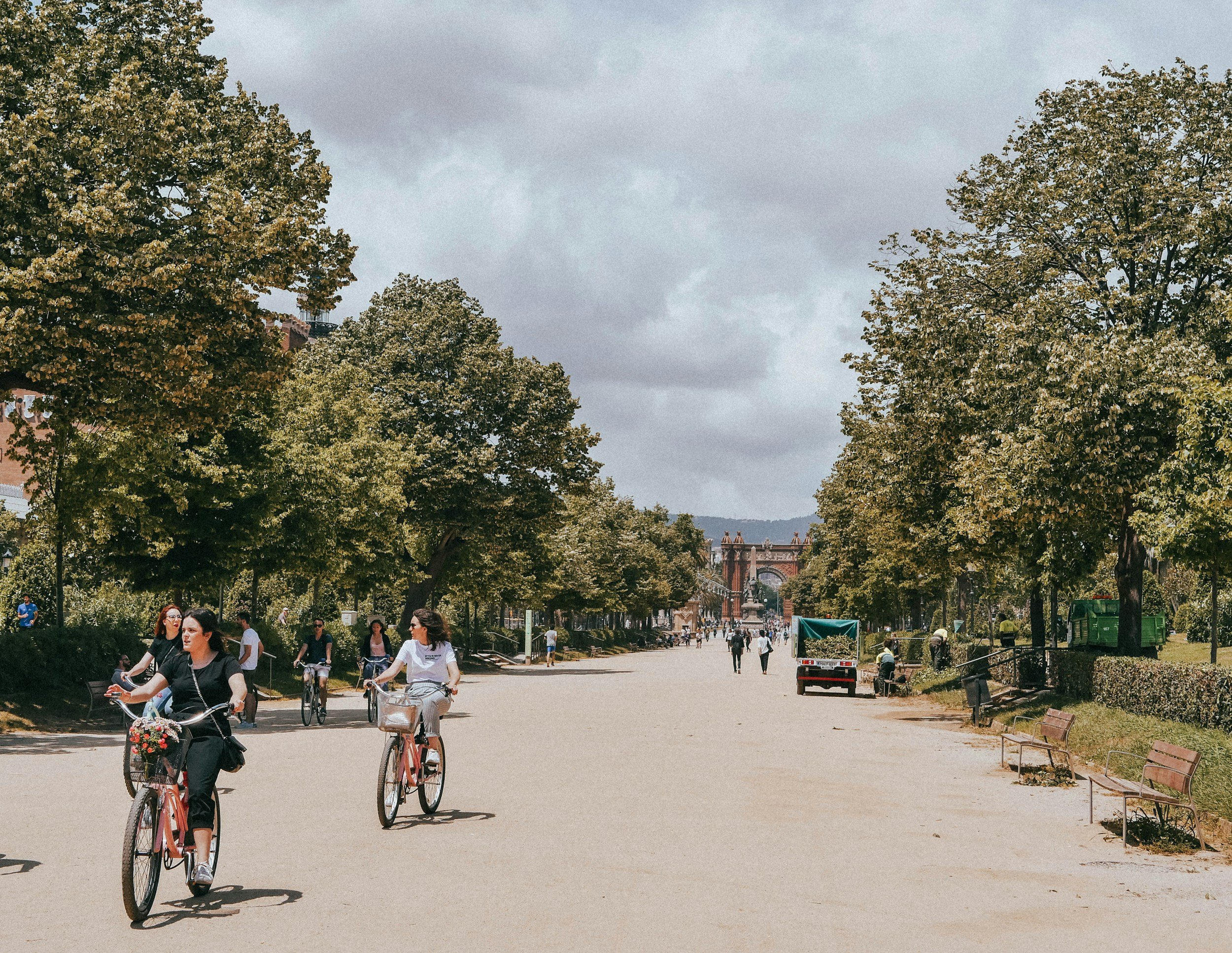 Selección de bicicletas de segunda mano en venta en la tienda Monbike en Barcelona, con una mujer circulando en bicicleta por el Parc de la Ciutadella.