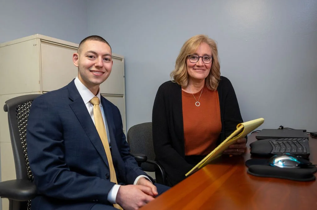 Rob and Carol sitting at a desk with a notepad, smiling