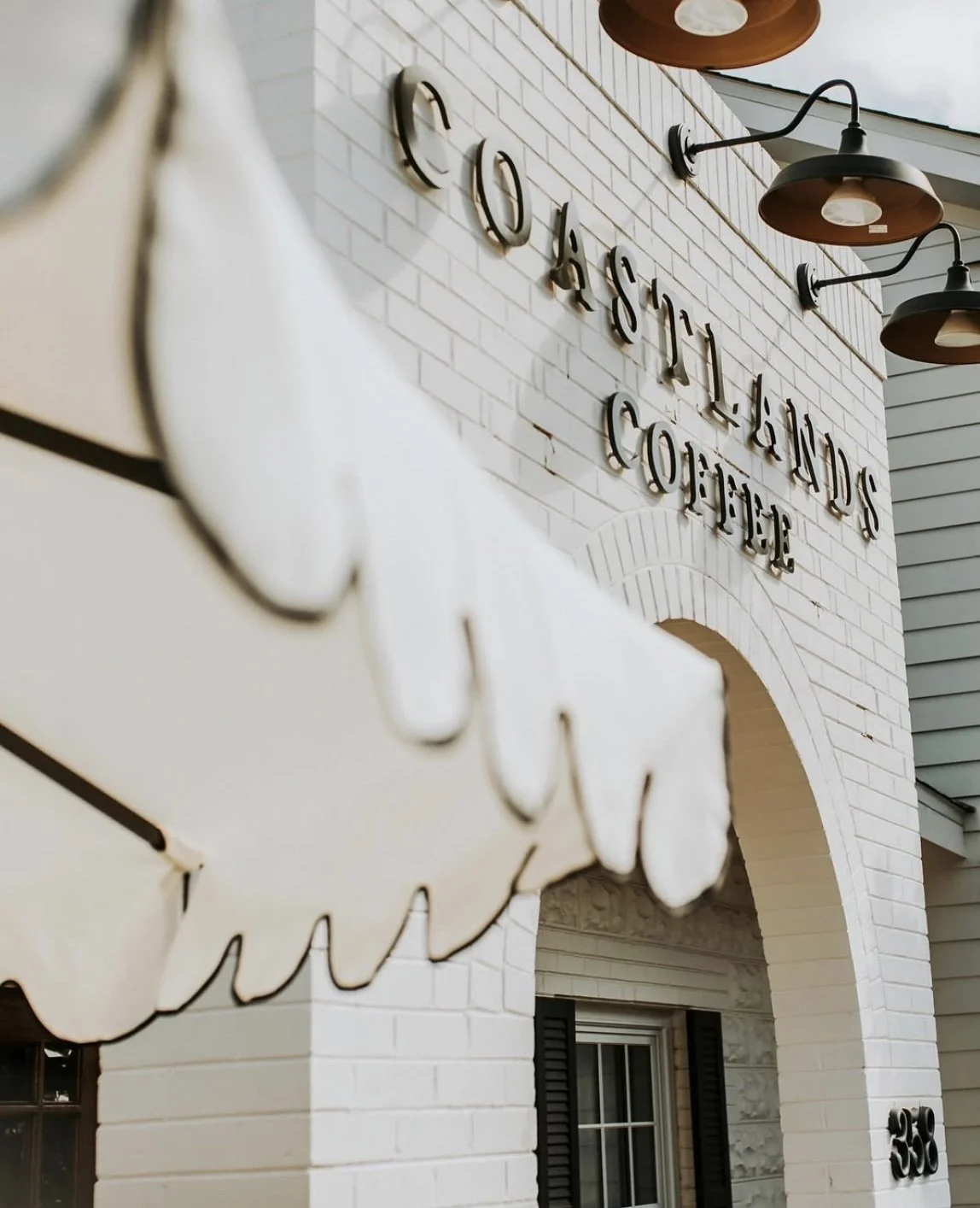 Close-up of a sign with the words 'COASTLANDS COFFEE' on a white brick building exterior.