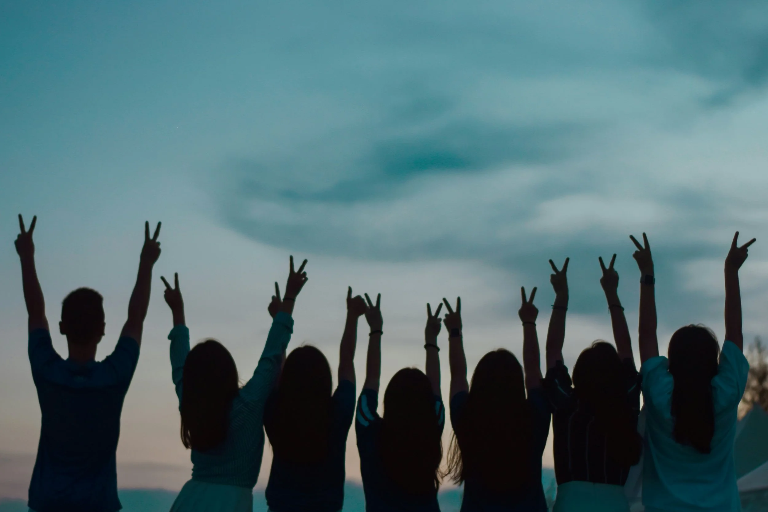 Group of children at the beach raising their hands with peace signs during sunset.