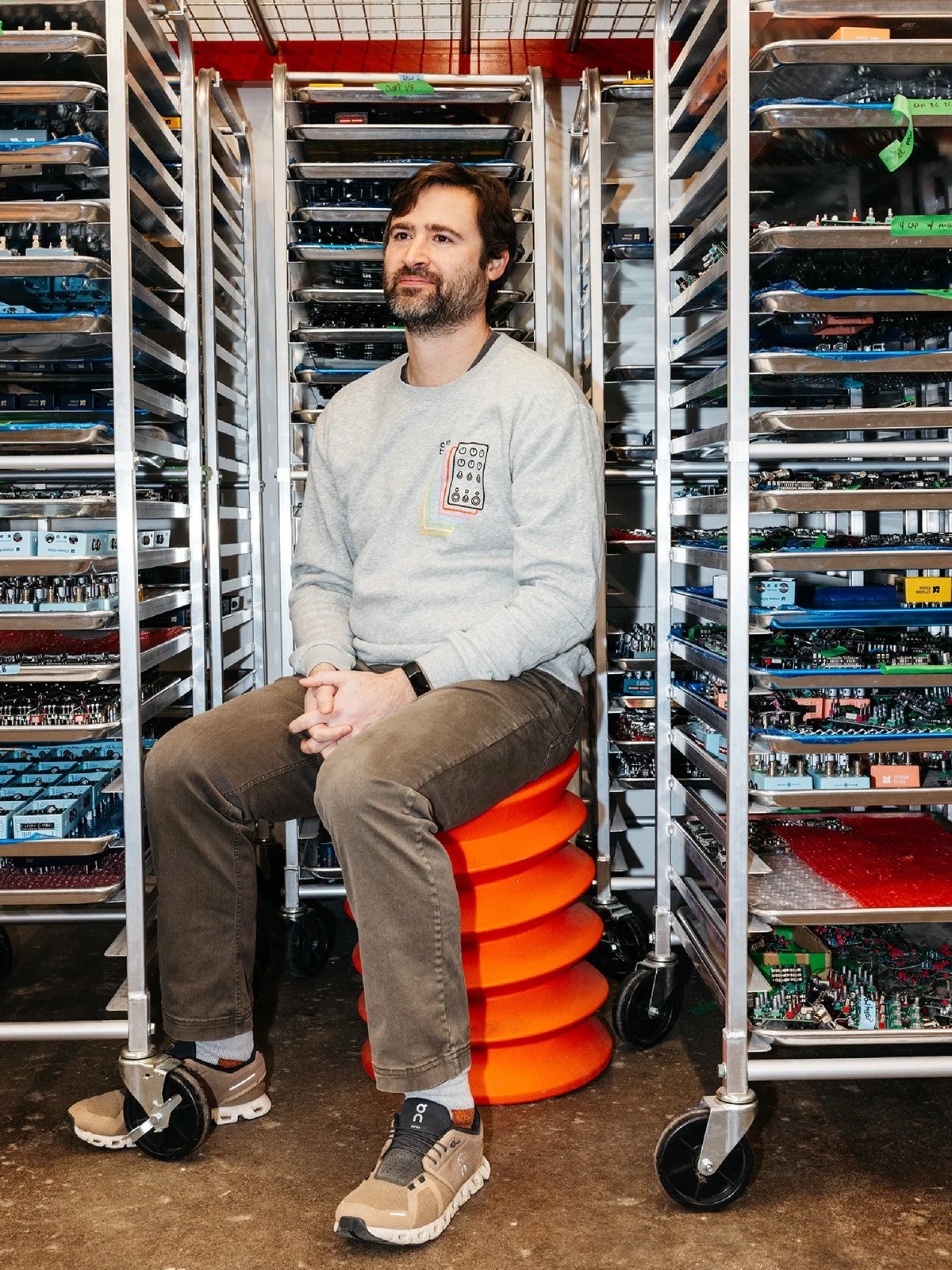 Person sitting (Joel Korte) surrounded by baking racks filled with guitar pedals.