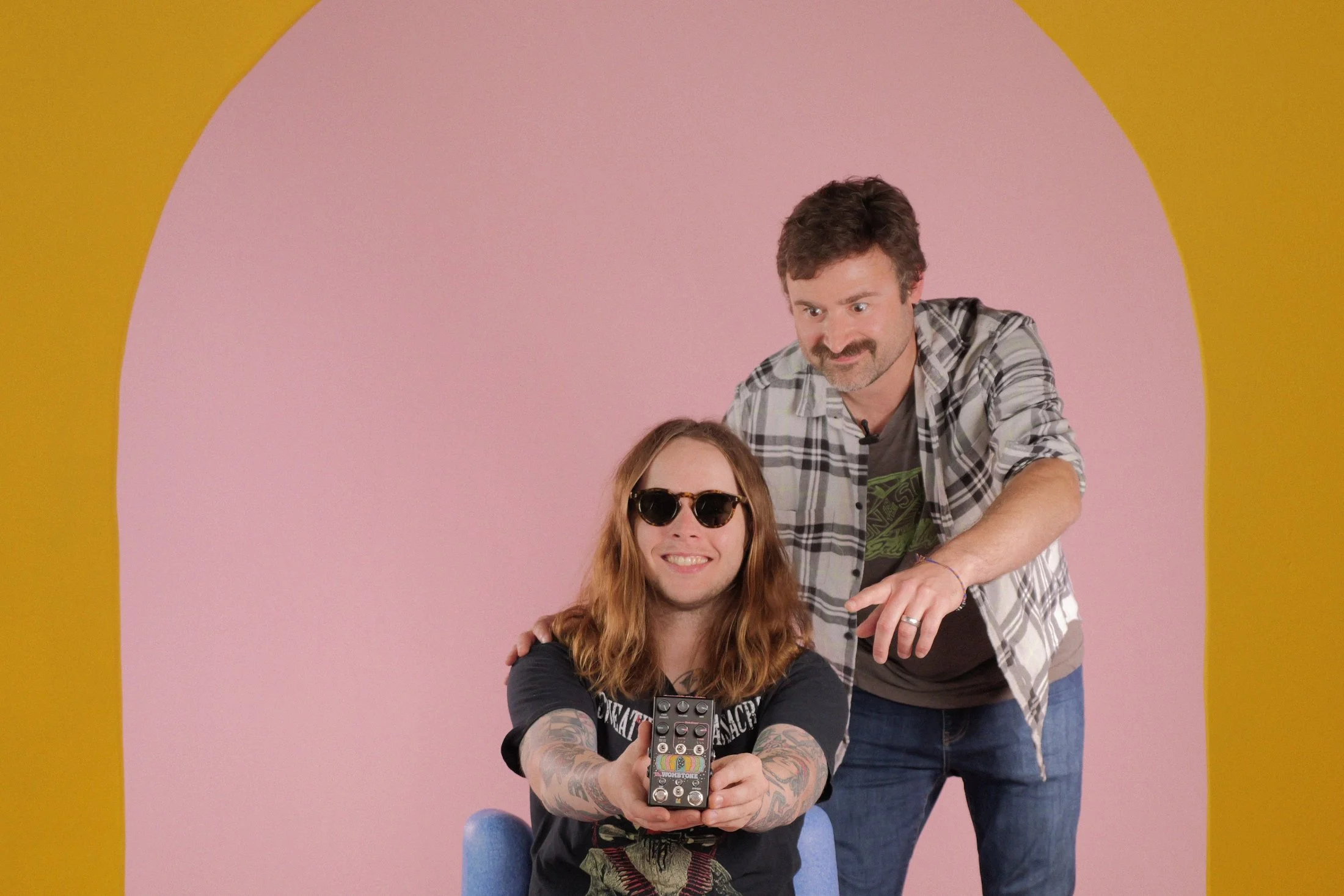 People (Joel Korte and Billy Strings) smiling and holding up the Billy Strings signature Wombtone effects pedal by Chase Bliss.