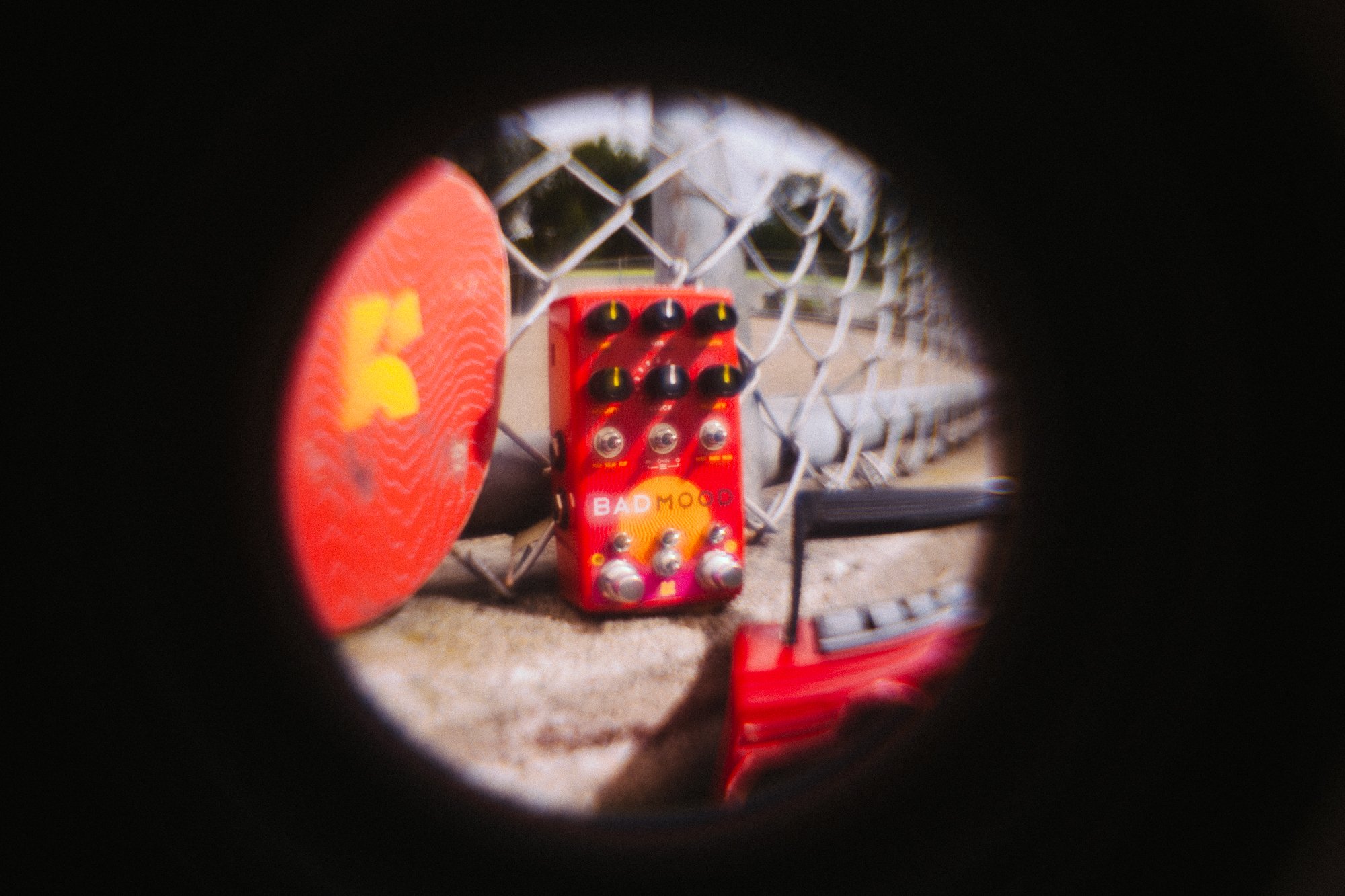 BAD MOOD leaning on a fence next to a skateboard and being seen through a fisheye lense.