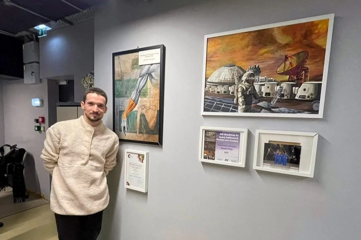 A man standing in an art gallery with framed artwork and certificates on the wall