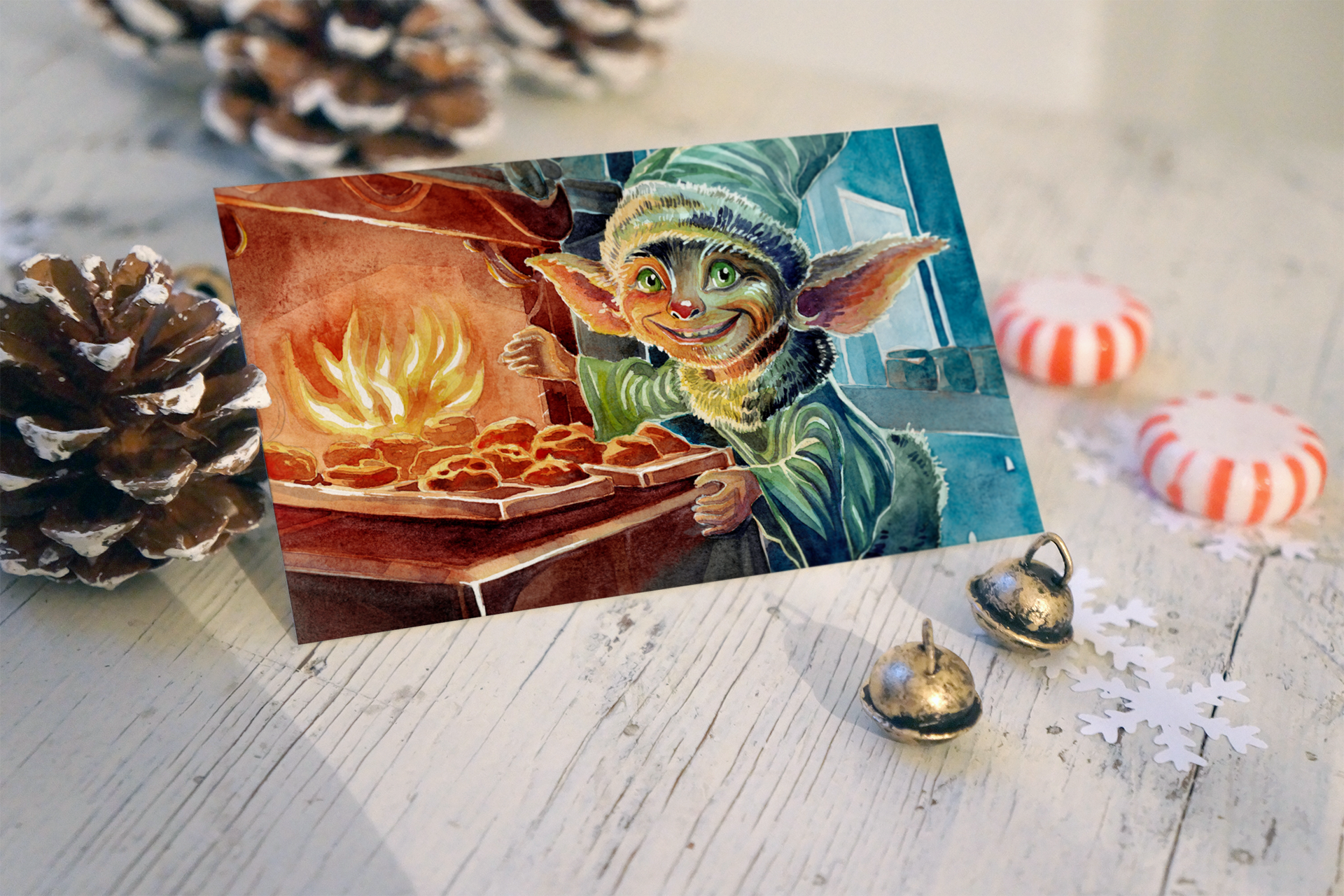 A holiday greeting card with an illustration of a cheerful elf in a cozy kitchen, baking cookies near a fireplace, surrounded by pinecones, ornaments, and paper snowflakes on a white wooden surface.