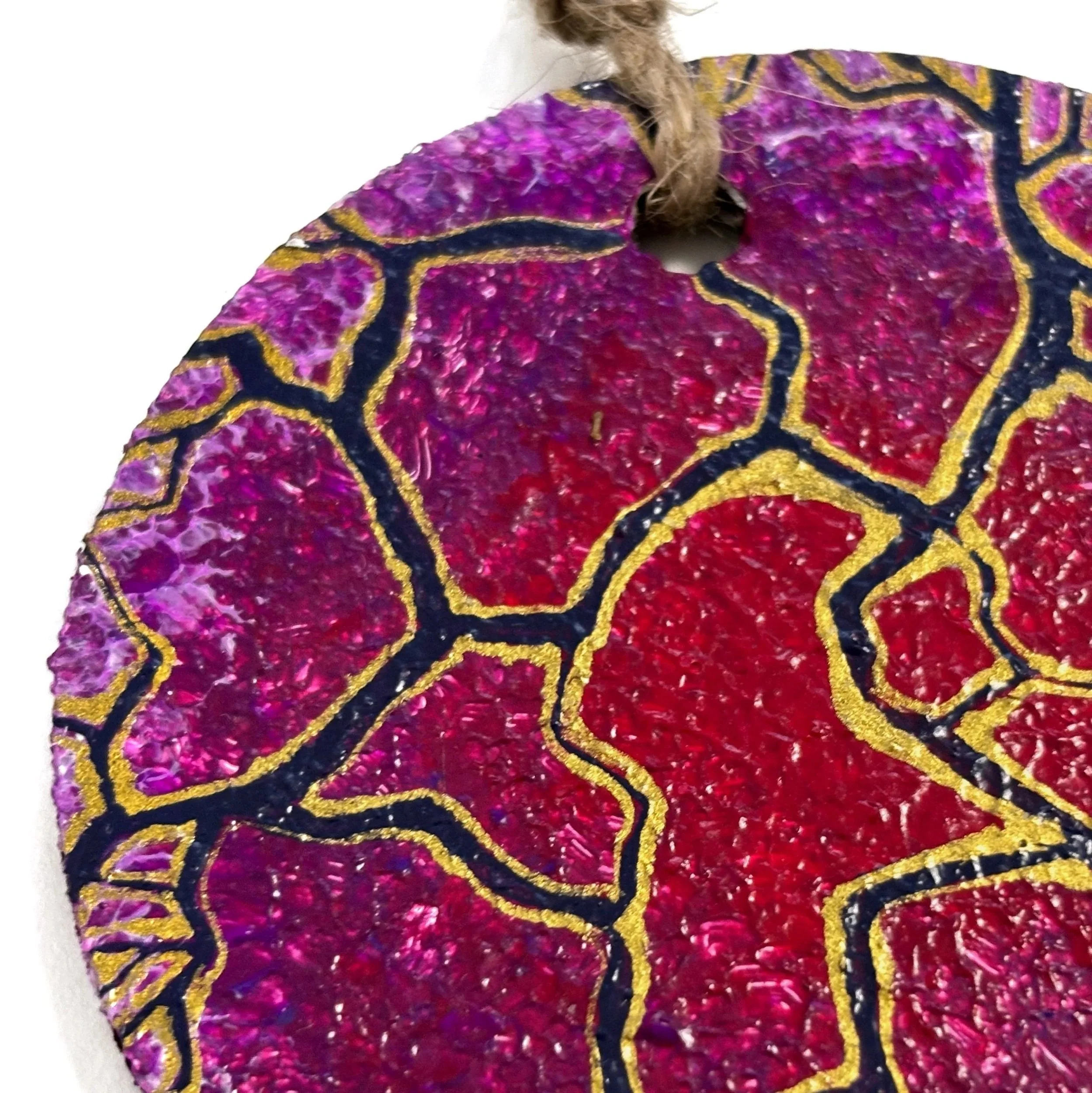 Prim-plan al unui obiect decorativ circular cu secțiuni texturate violet și roșii, conturate cu negru și auriu.