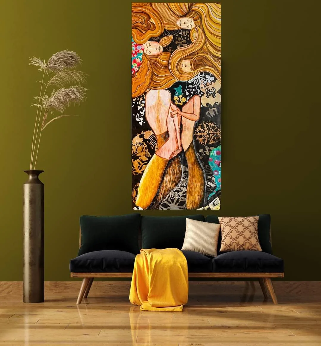 A modern living room with a green wall, a black velvet sofa with three pillows and a yellow blanket, a tall gold vase with pampas grass to the left, and a colorful abstract painting featuring female figures and intricate patterns hanging above the so