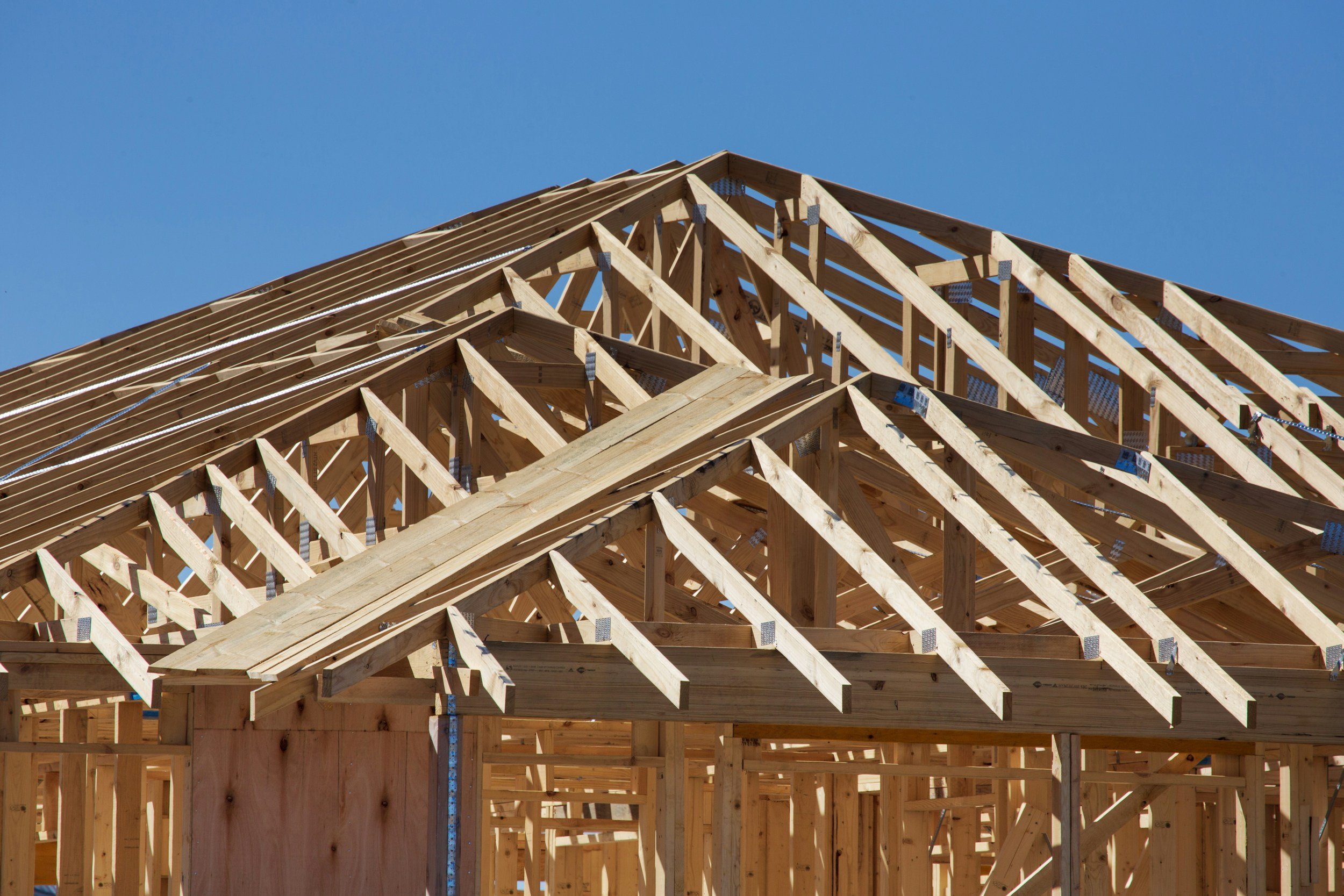 Wooden house framing under construction against a clear blue sky.