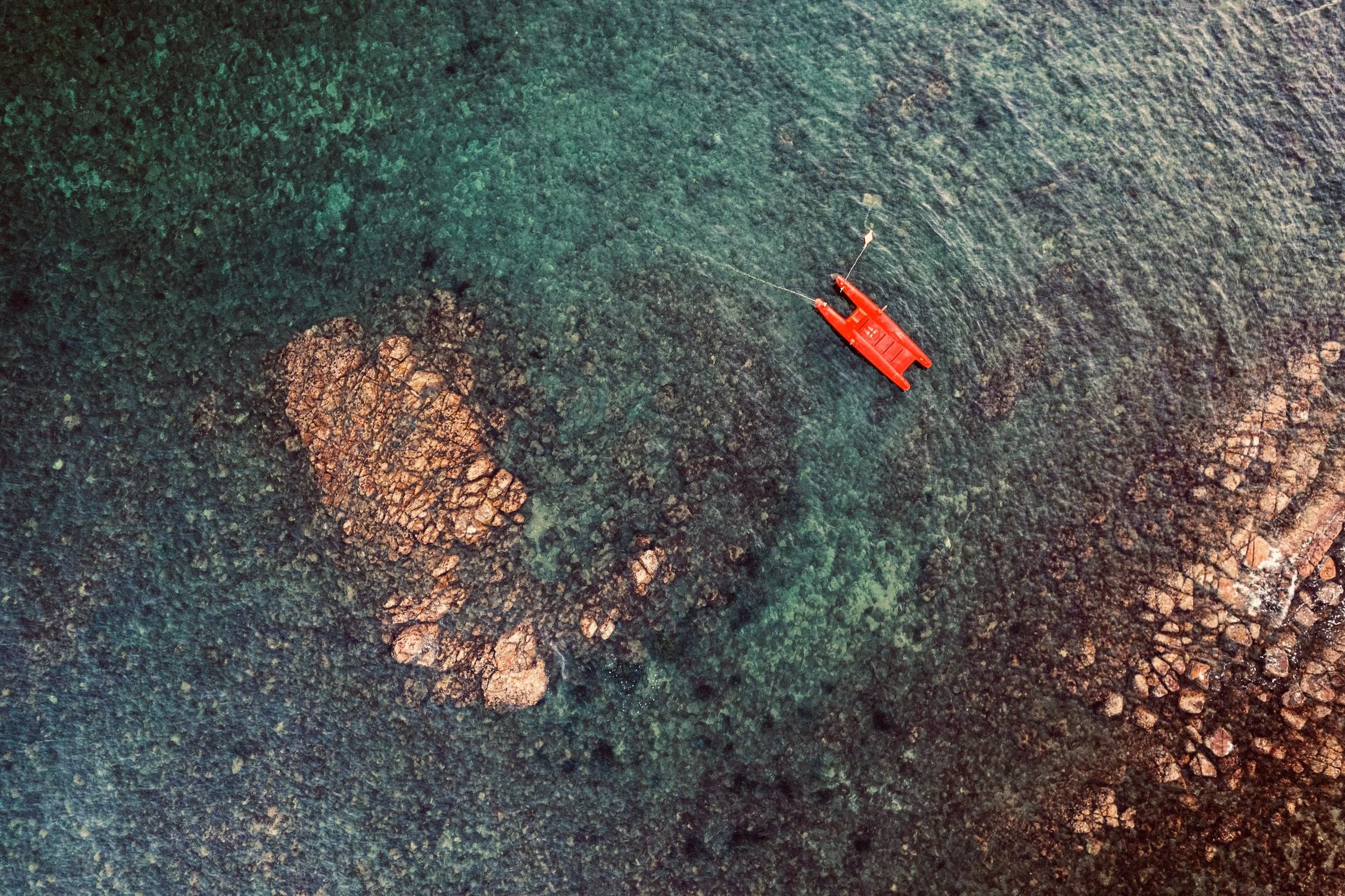 Immagine aerea di una barca rossa in mare vicino a una costa rocciosa con acqua trasparente