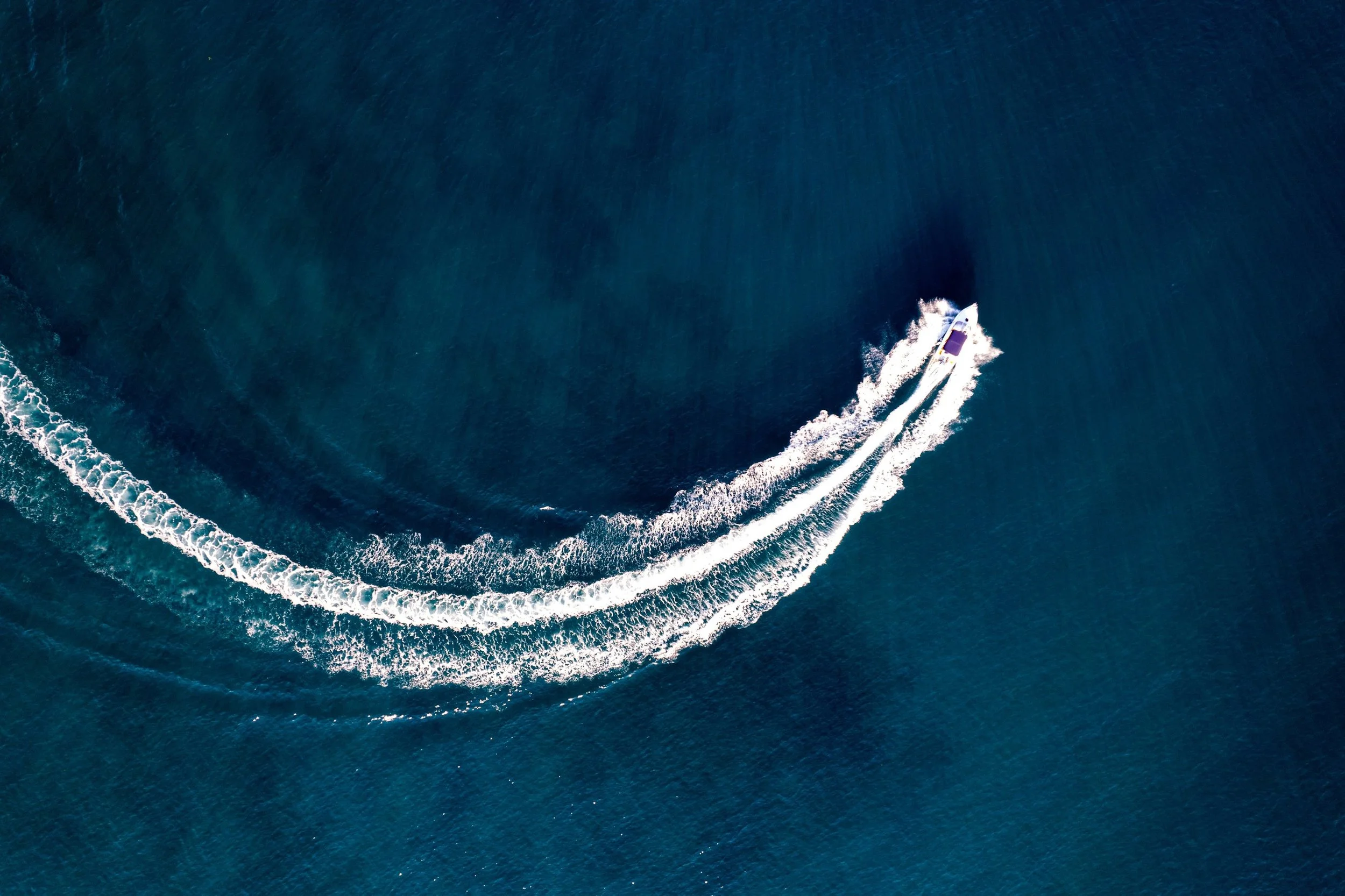 Una barca a motore che attraversa il mare, lasciando una scia di schiuma bianca nell'acqua blu.