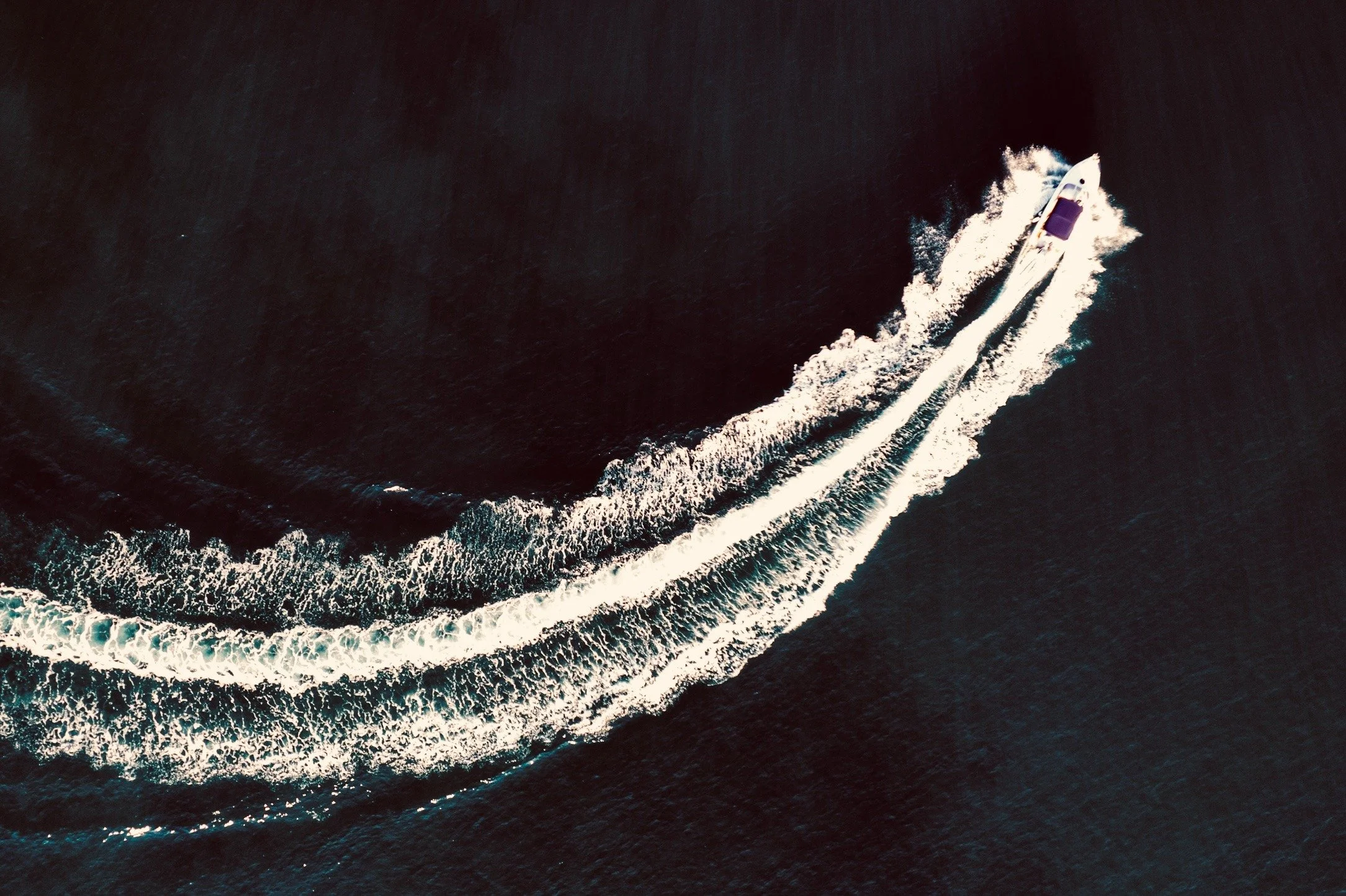 Veduta aerea di uno yacht che naviga sull'oceano, lasciando una lunga scia di onde.