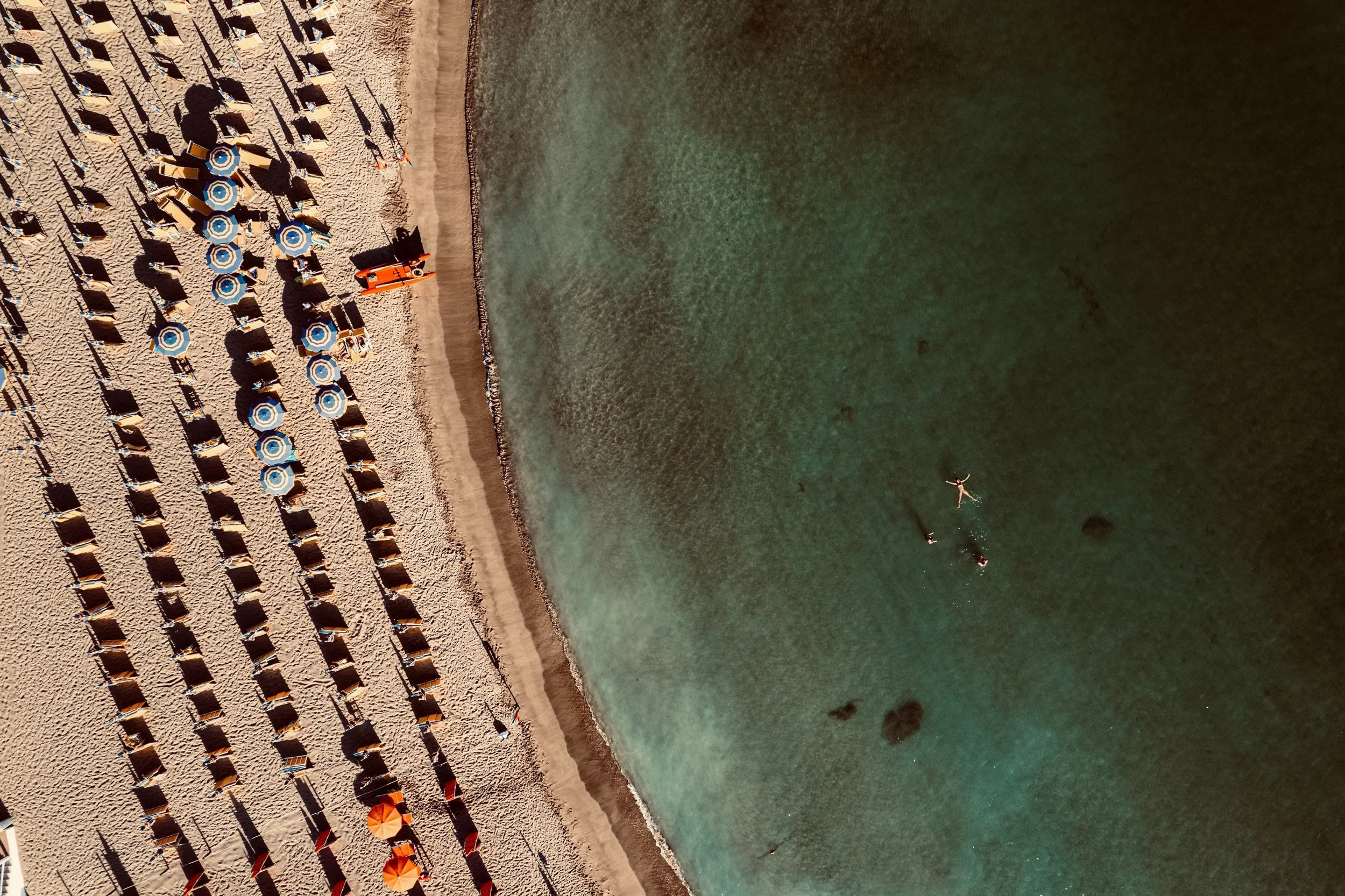 Spiaggia con cabine e ombrelloni, acque chiare con persone che nuotano e fanno snorkeling.