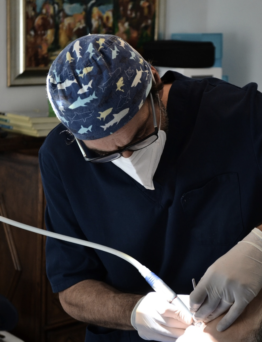 Un medico che lavora su un paziente, indossa casco, mascherina e occhiali, con attrezzature mediche nell'ambiente.