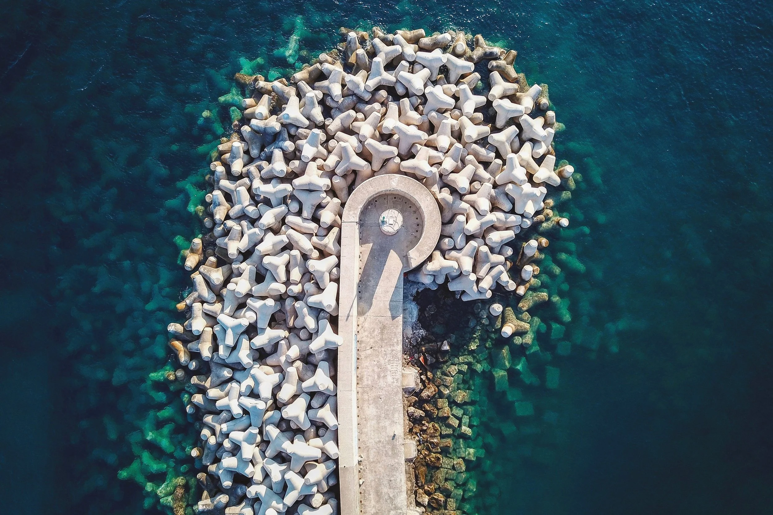 Veduta aerea di un molo con strutture di elementi in cemento che si estende nel mare blu con acque trasparenti