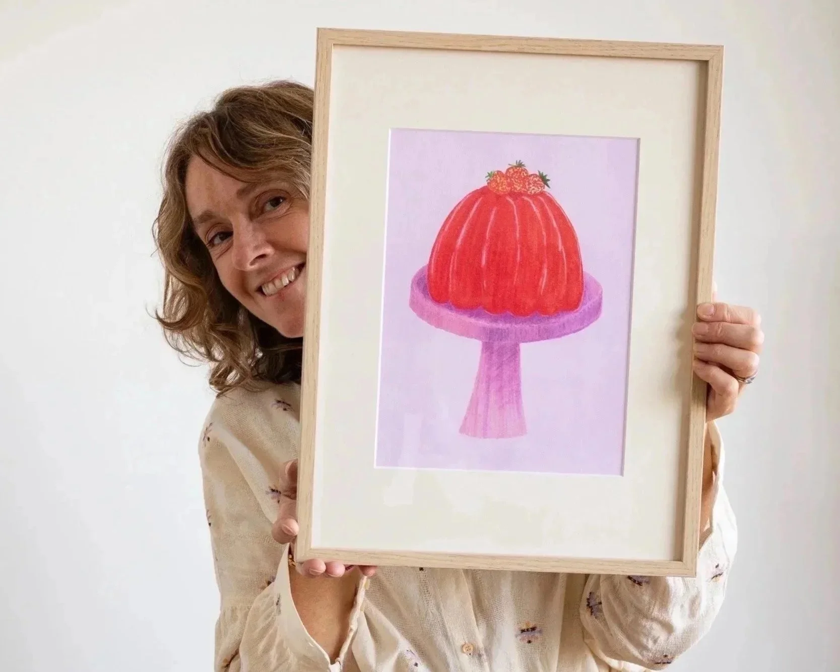 Clare Jones Paris based illustrator smiling and holding her framed Strawberry Jelly art print.