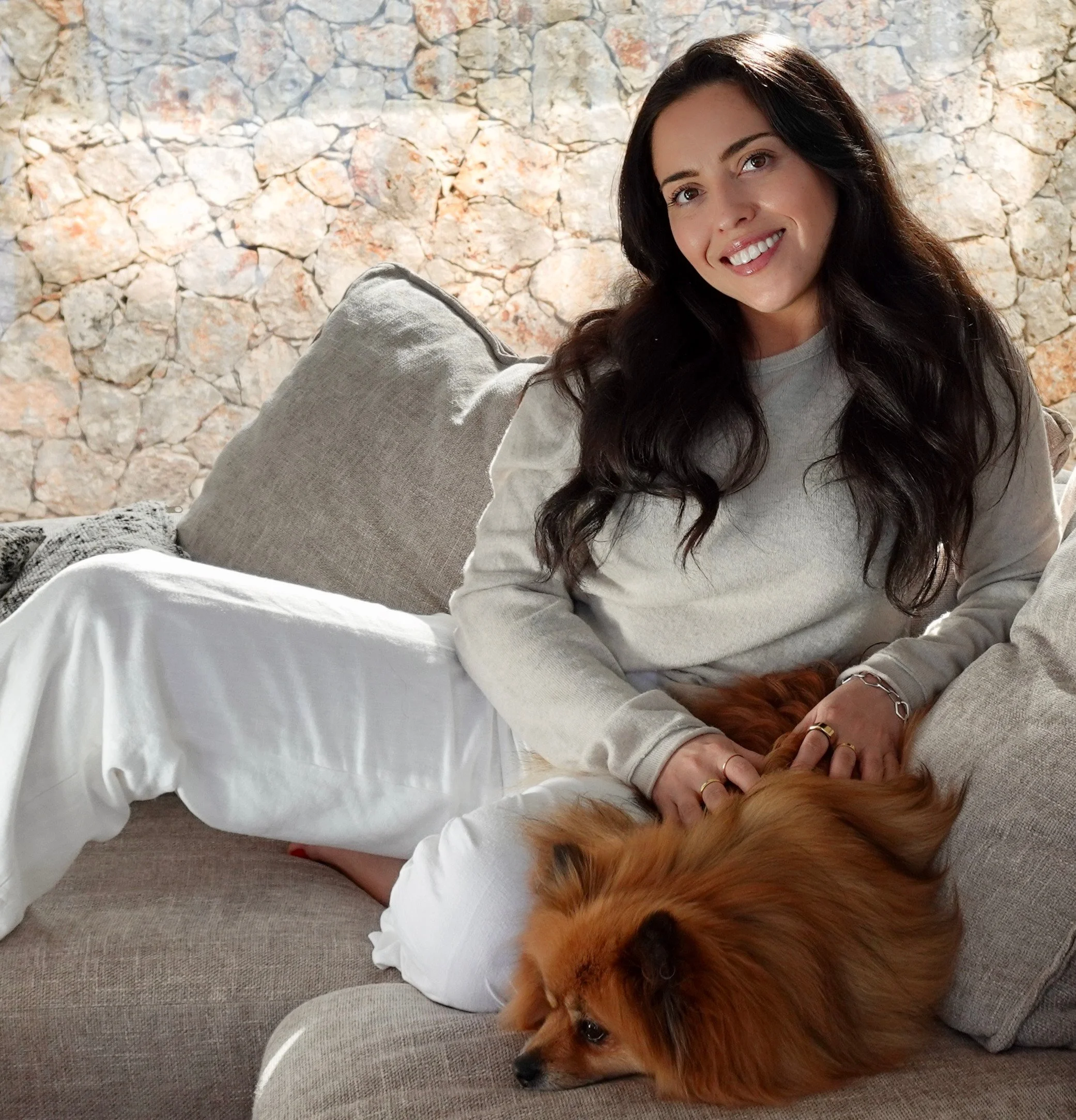 Antoinette sitting on a grey couch with a Pomeranian