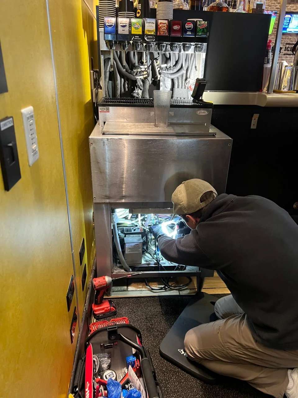 AirNest Service technician repairing a soda fountain unit behind a bar