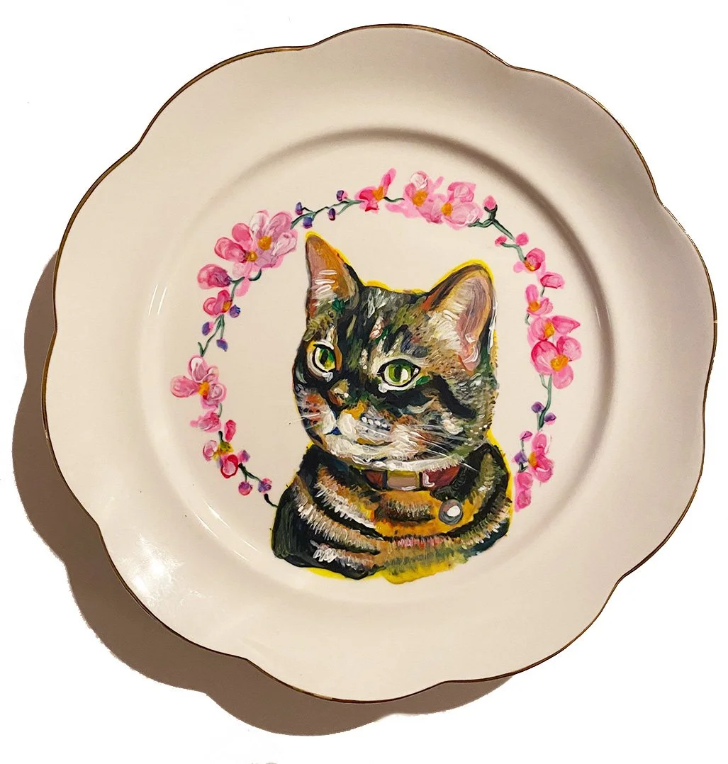 Decorative plate featuring a painted portrait of a tabby cat with green eyes, a collar with a bell, and surrounded by a pink floral wreath.