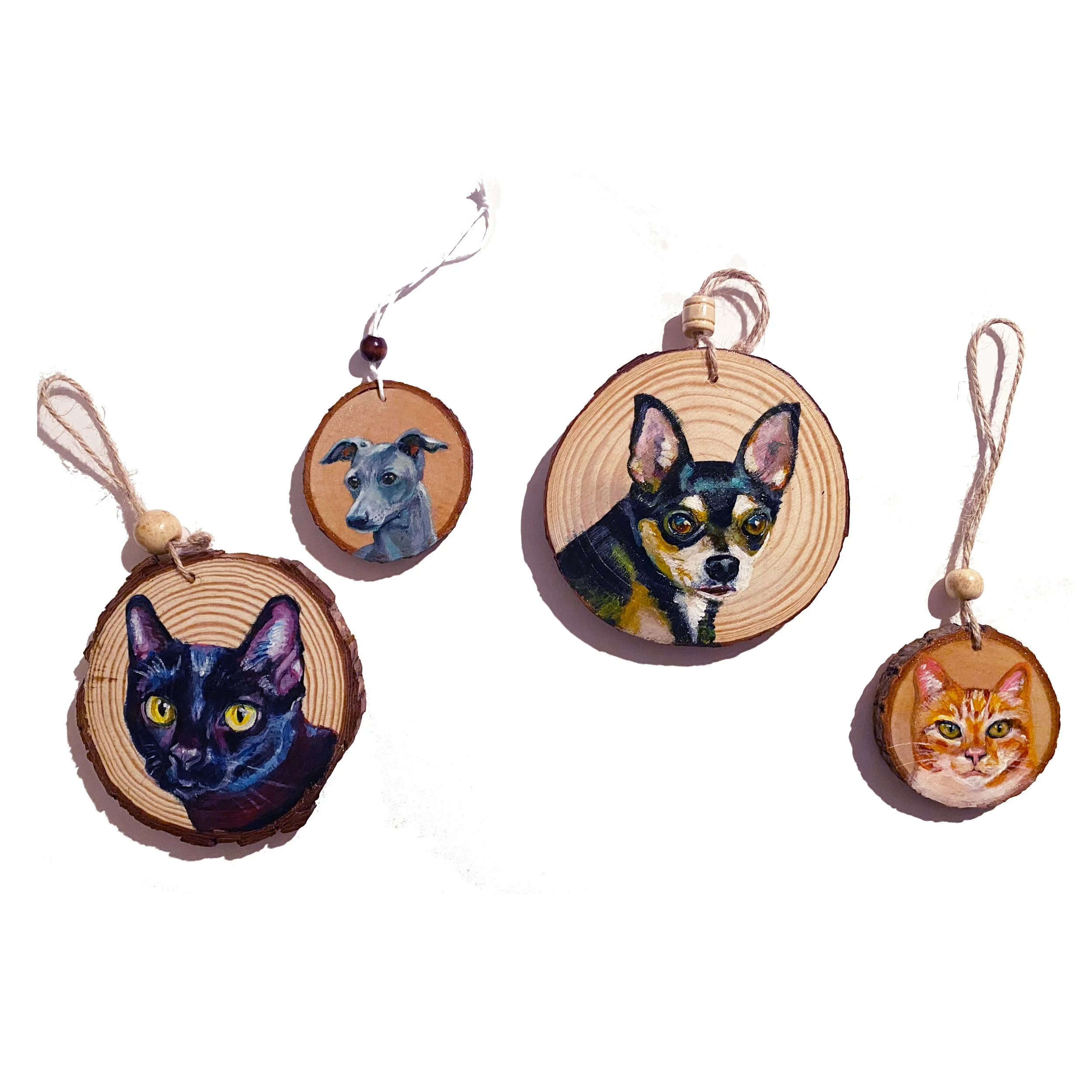 Wooden ornaments with painted portraits of pets, including a cat, two dogs, and a cat, hung on strings.