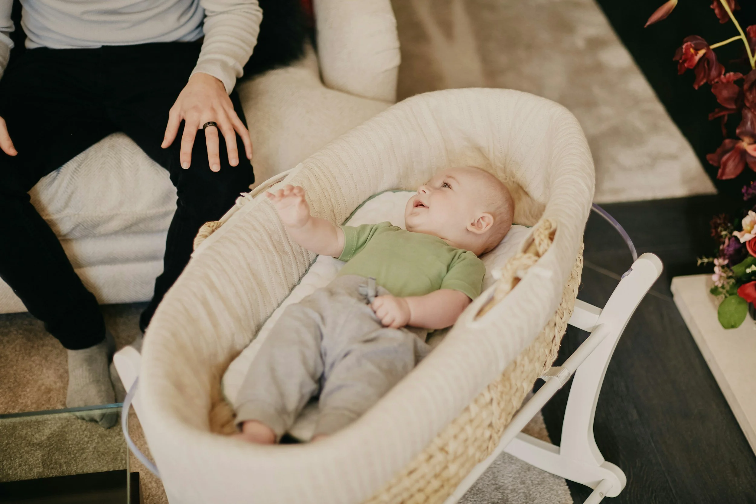 A baby in a bassinet in a green shirt next to a parent