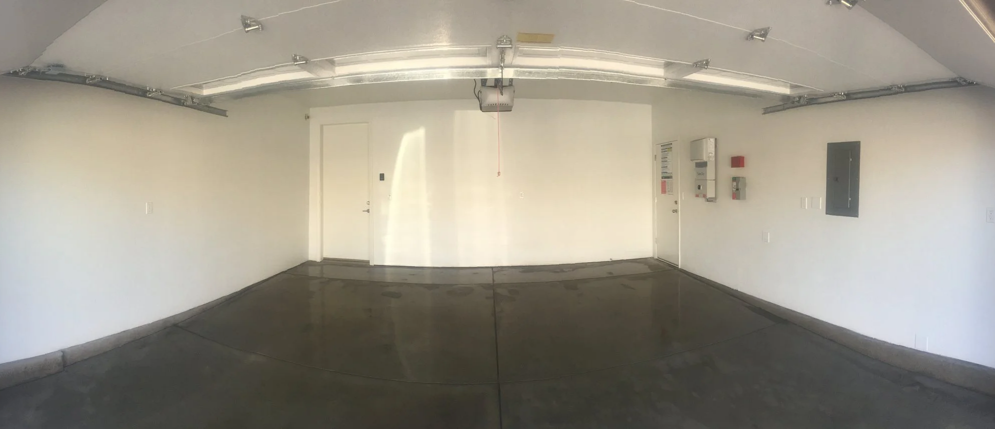 Empty residential garage with white walls, concrete floor, garage door on ceiling, and various utility boxes on wall.