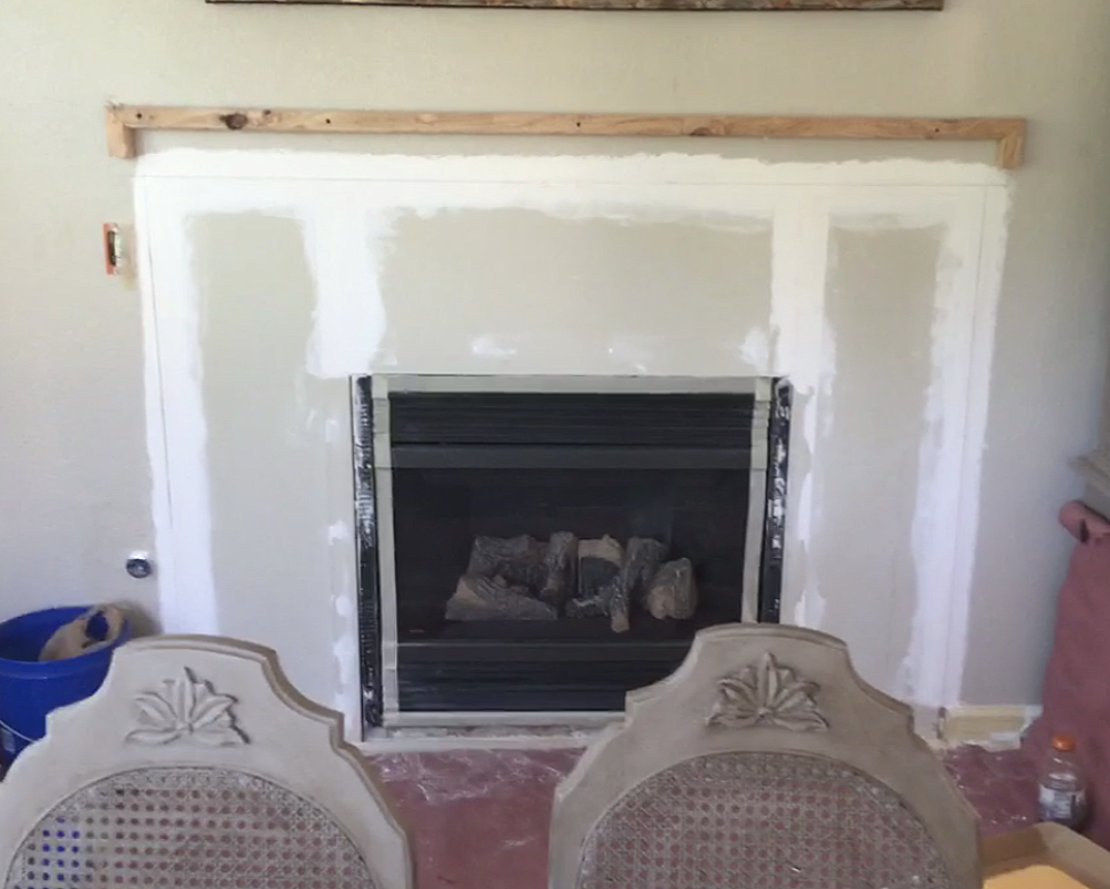 Room under renovation with a fireplace framed in drywall, with rocks and debris inside, and two chairs with carved backs in the foreground.