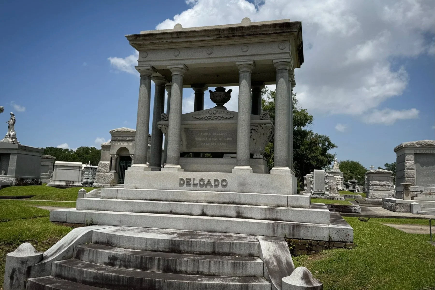 Monumental Delgado family tomb with broad steps and granite columns at Metairie Cemetery in New Orleans.