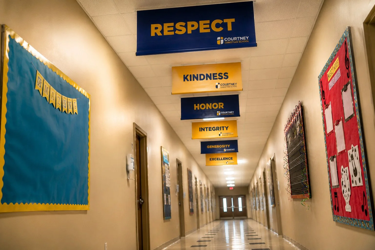 School hallway with banners hanging from the ceiling that read "Respect," "Kindness," "Honor," "Integrity," "Generosity," and "Excellence." On the walls, bulletin boards display various colorful decorations and student work.