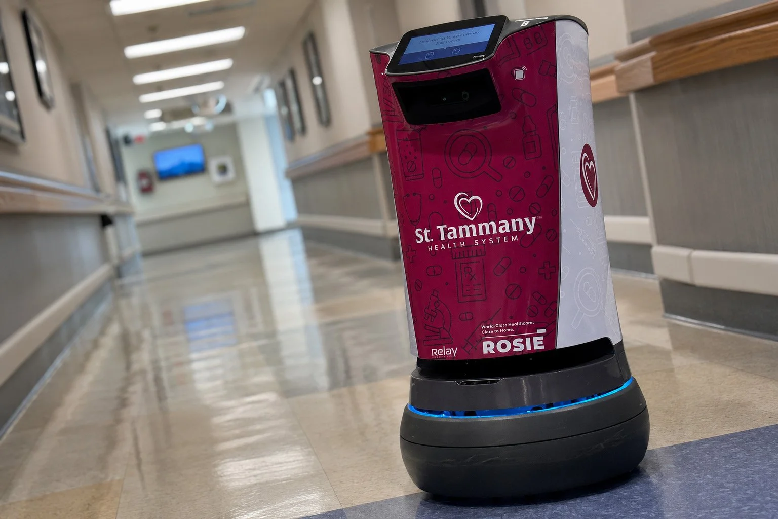 ROSIE, a burgundy-and-gray St. Tammany Health System autonomous courier robot, traveling through a hospital corridor.
