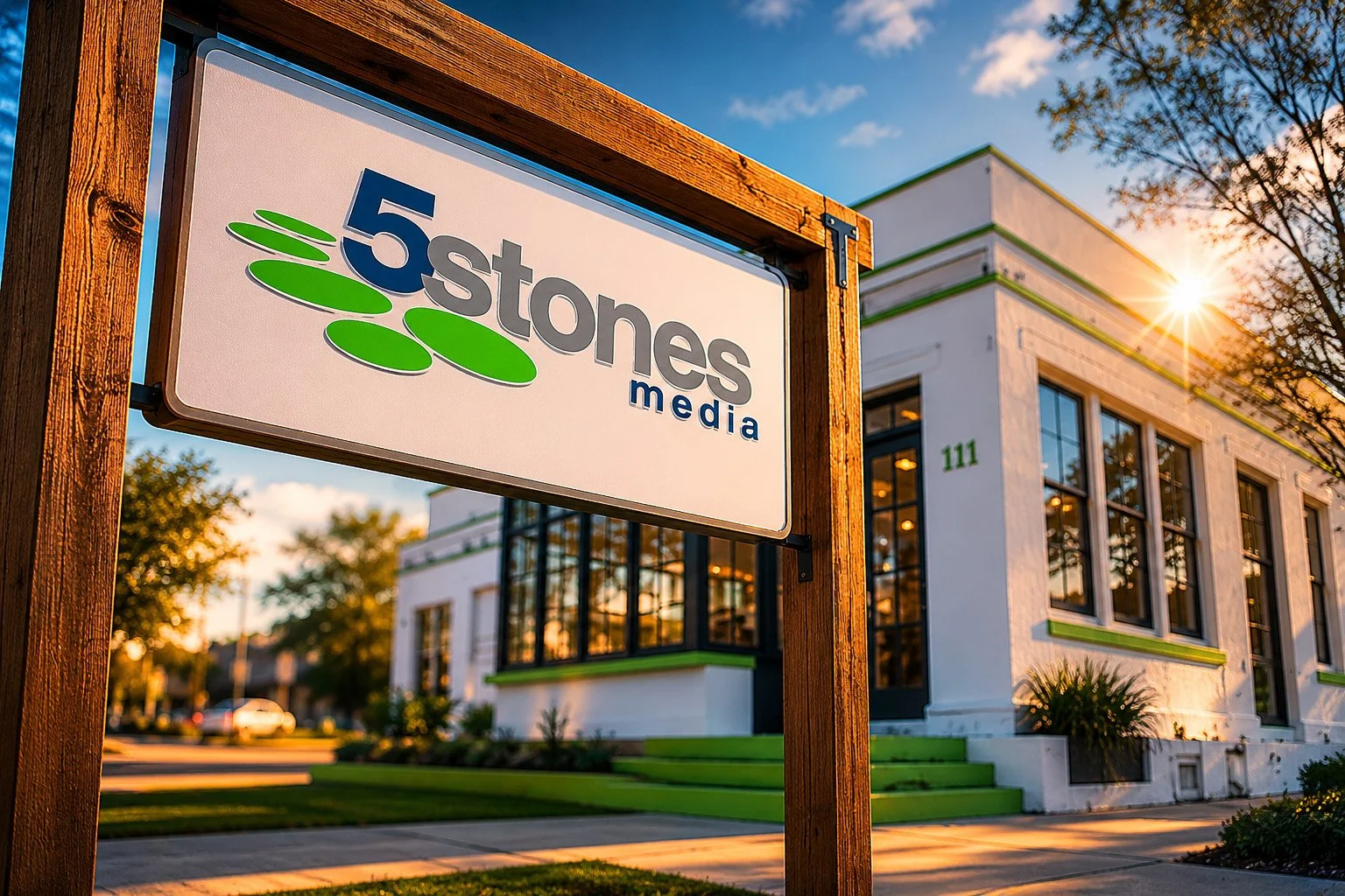 Sign for 5 Stones Media in front of a modern white building with large windows, set in a sunny neighborhood with trees and a well-kept lawn.