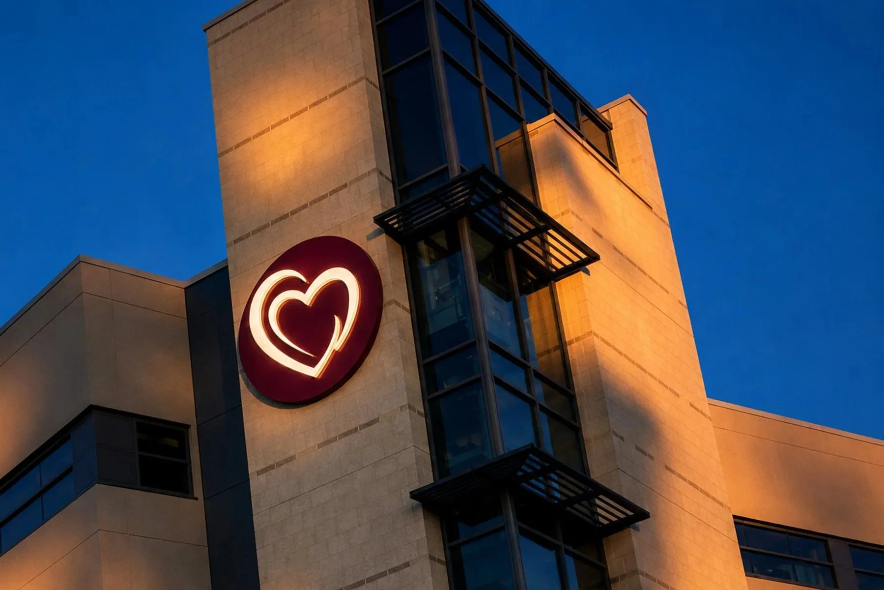 St. Tammany Health System’s illuminated interlocking hearts mounted on the South Tower against a deep blue evening sky.
