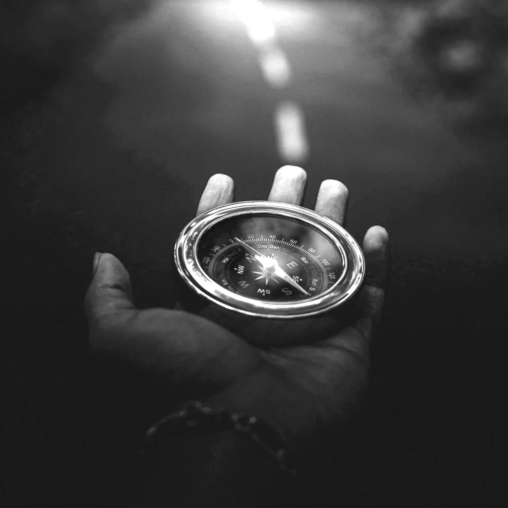 Black-and-white photograph of hands holding a reflective sphere outdoors.