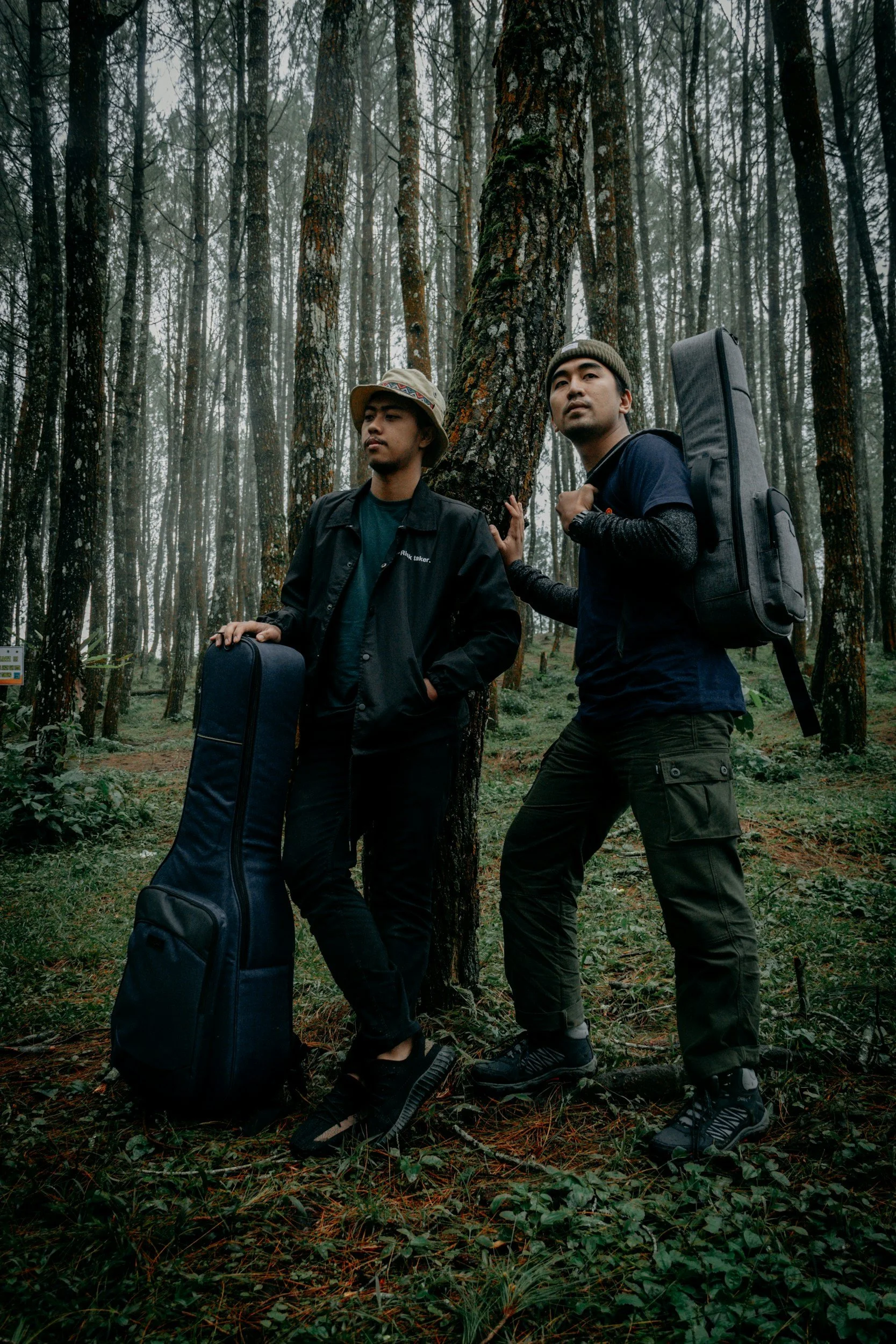 Grounded Media - Two men with packed musical instruments in a misty forest, leaning against a tree.