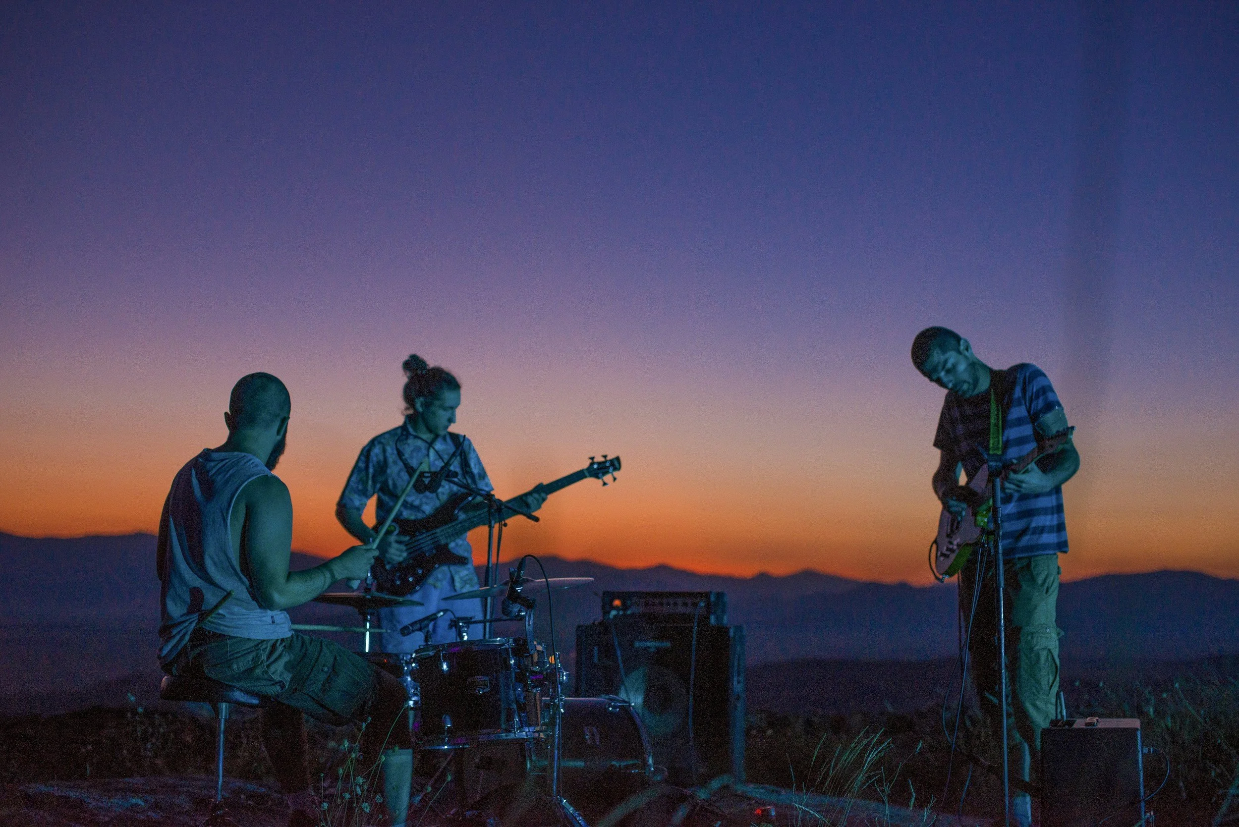 Grounded Media - Three musicians playing instruments outdoors during sunset, with mountains in the background.