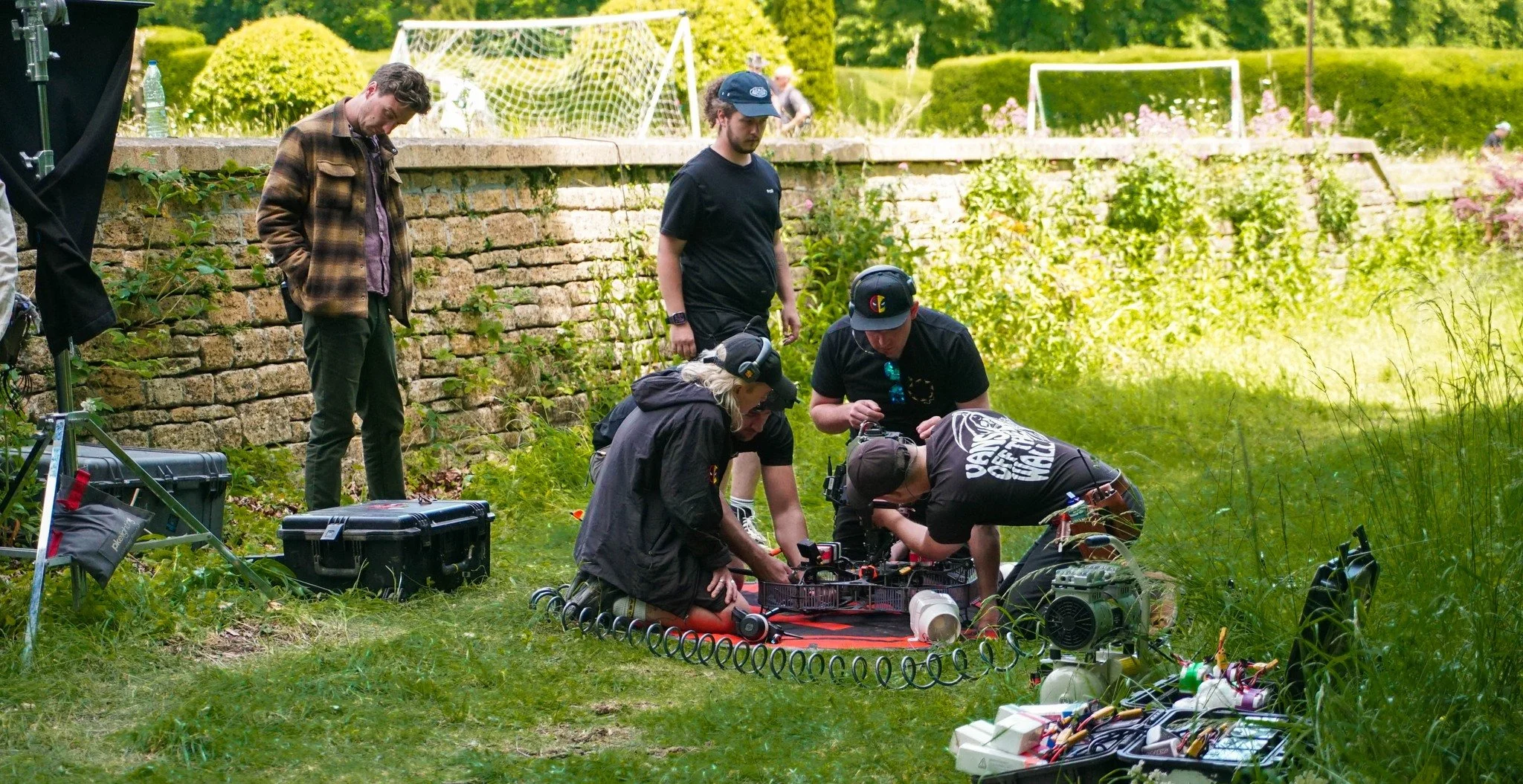 Stan Thornton and a team of people working with technical drone equipment outdoors near a stone wall and lush greenery, on the film set of Steve (2025)