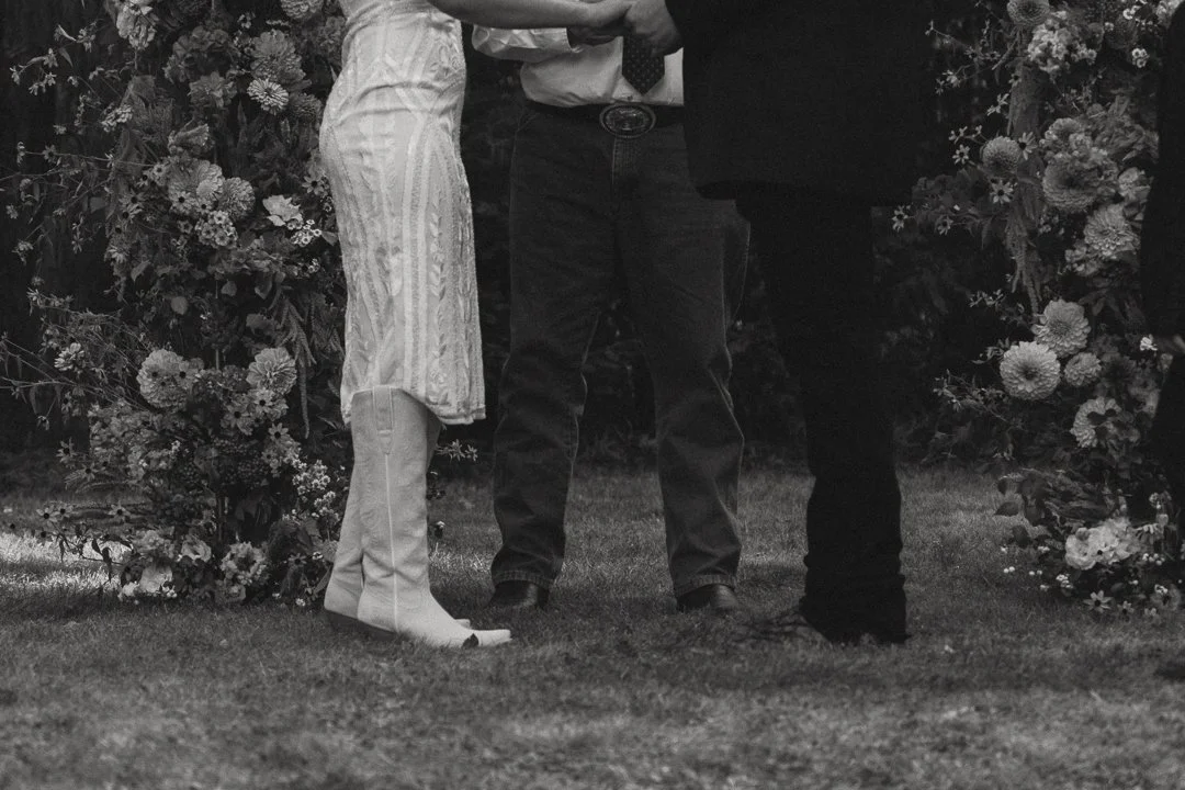 A couple is exchanging rings at a wedding ceremony, with an officiant present. The scene is decorated with flowers.