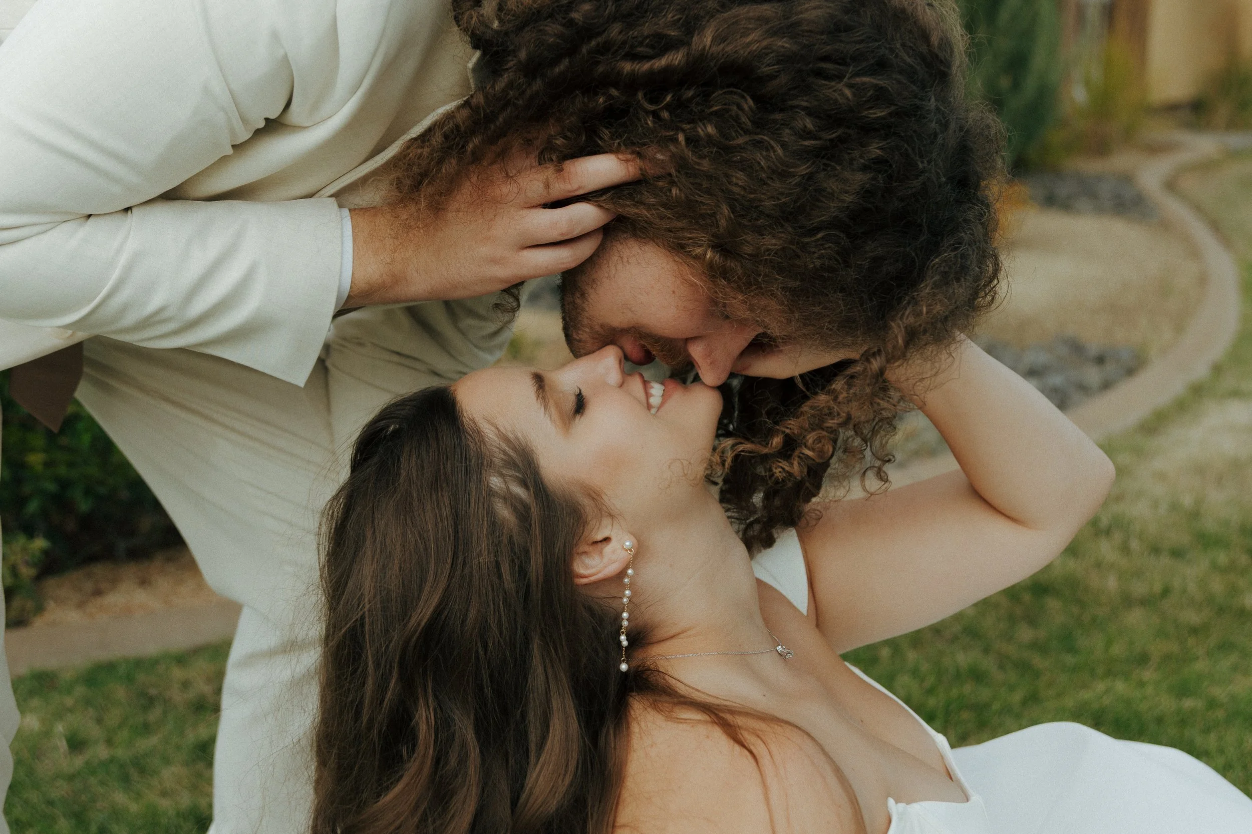 A couple sharing an intimate moment outdoors, faces close together, with the woman lying on her back and the man leaning over her.