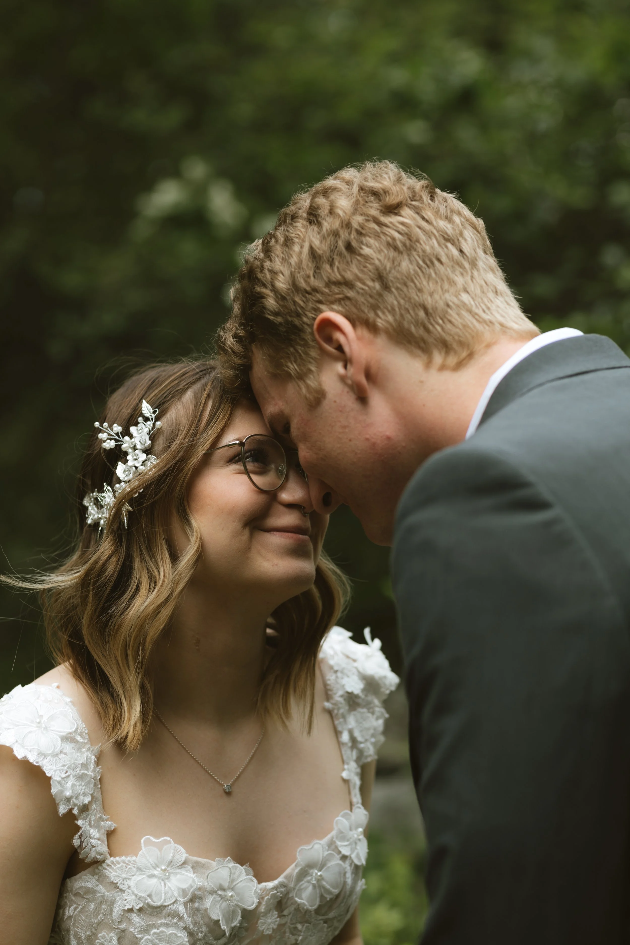 A couple is sharing a close, intimate moment outdoors, with their foreheads touching.