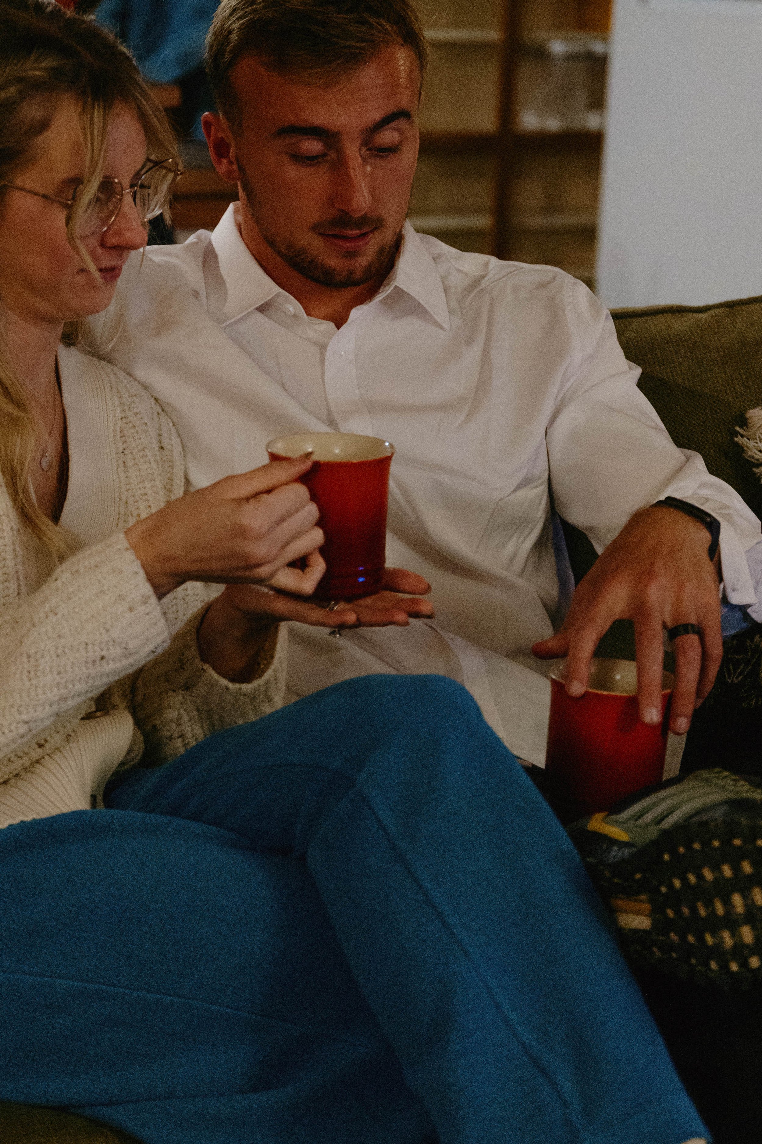 A man and a woman sitting on a couch, holding red cups, enjoying a cozy moment together.